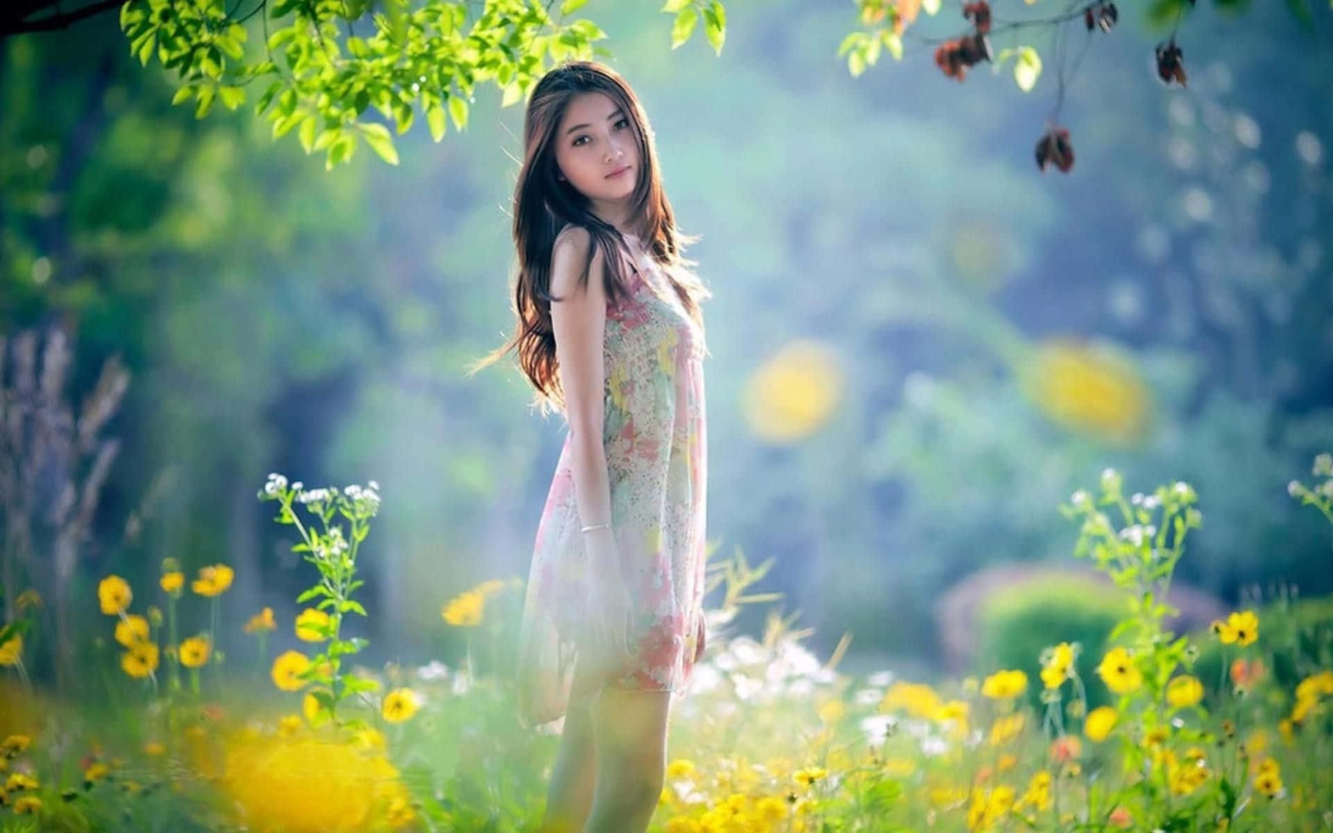 Beautiful Girls 桌布 壁紙 — 一位身穿花卉連衣裙的年輕女子，在斑駁的綠樹下，優雅地站在陽光普照的黃色野花叢中。