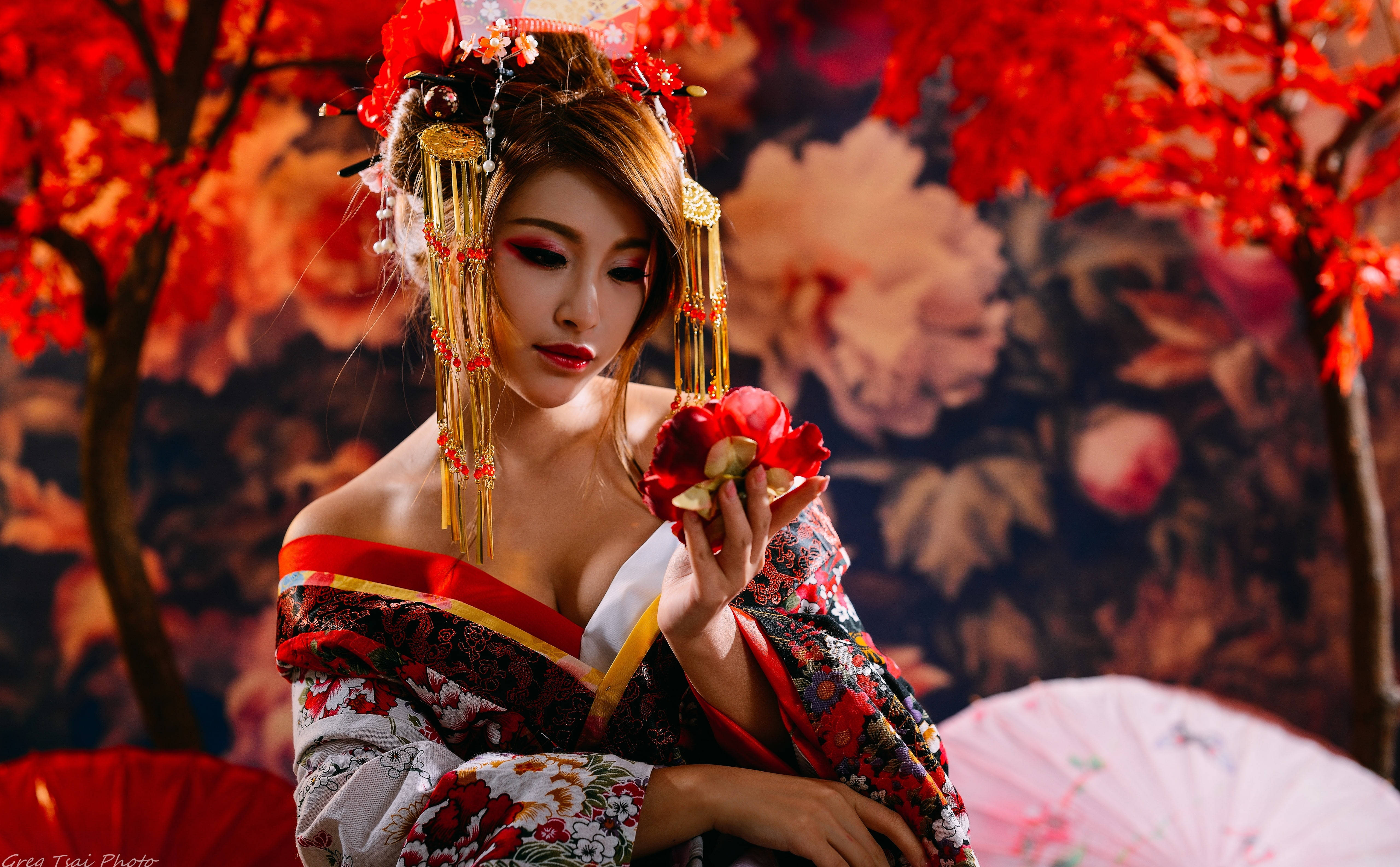 日式 桌布 壁紙 — 一位身穿華麗傳統日本服飾的女性，在色彩繽紛的秋樹下持著一朵紅花。