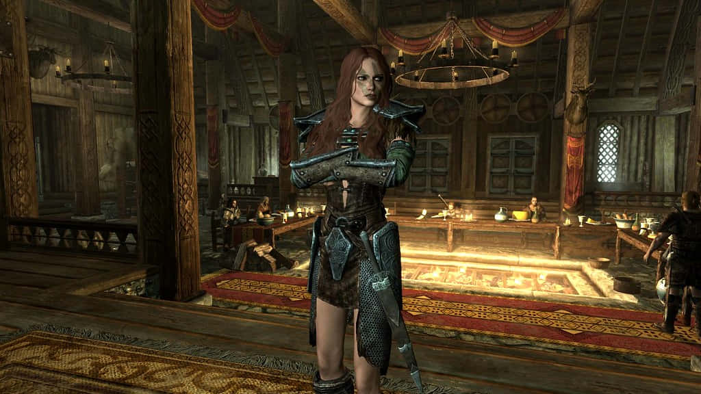 Aela The Huntress 桌布 壁紙 — 一位身穿華麗盔甲的女戰士站在光線昏暗的中世紀大廳中，大廳有木樑和中央火坑。