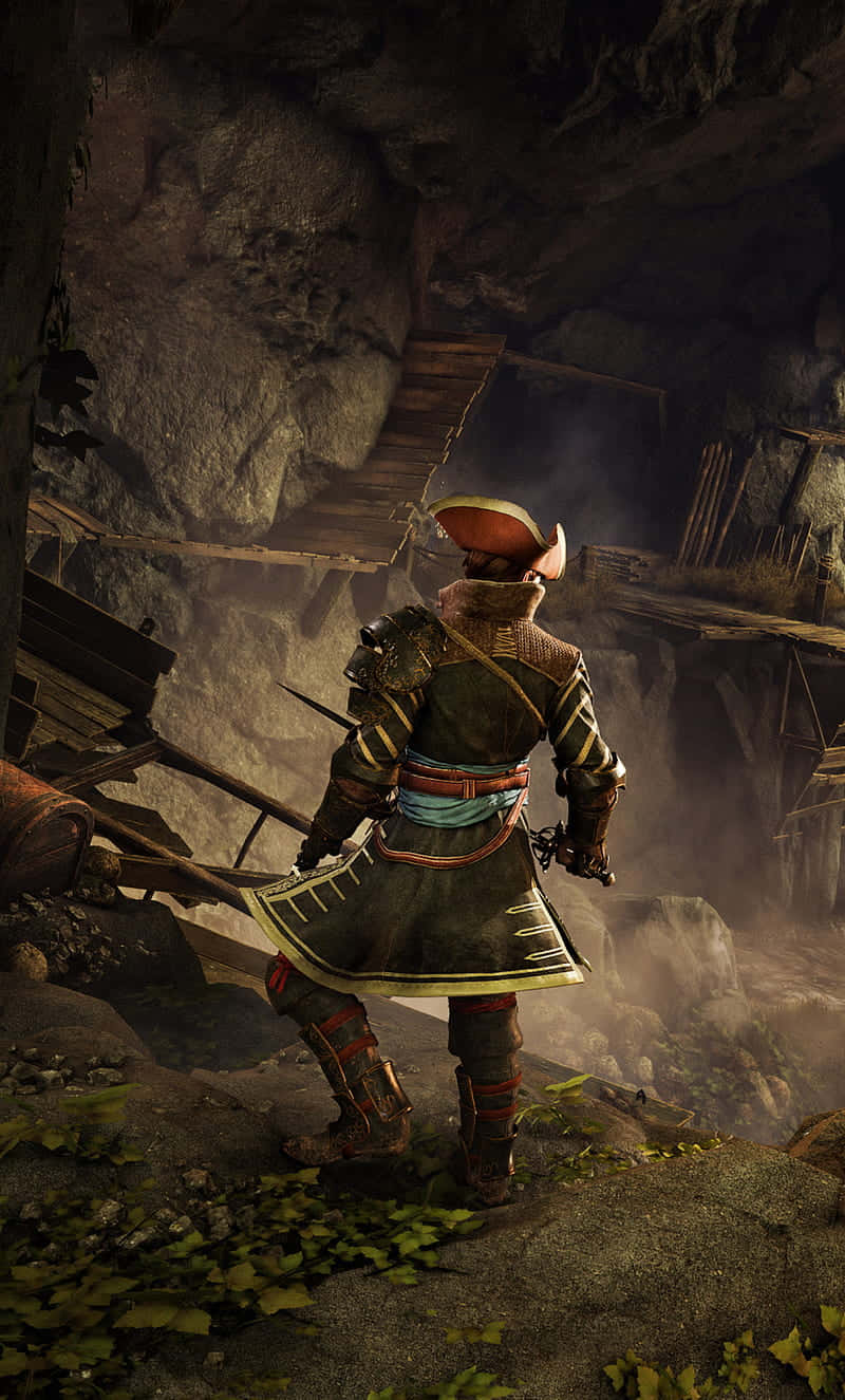Android Greedfall 桌布 壁紙 — 一位身穿華麗盔甲的武士站在岩石峭壁上，俯瞰著一個迷霧籠罩、破敗的木結構建築，該建築坐落在洞穴般的懸崖中。