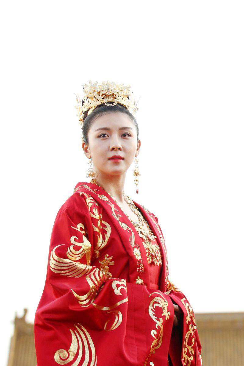 kdrama 桌布 壁紙 — 一位身穿華麗紅色傳統長袍、飾有金色鳳凰刺繡和華麗冠冕的女性，站在明亮的白色背景前。
