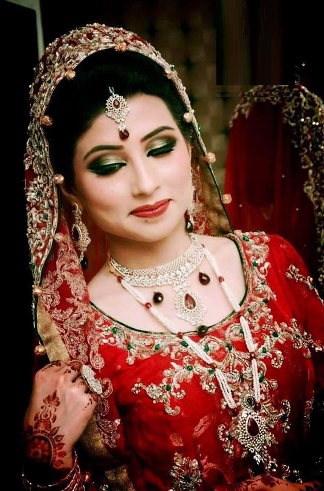 Bride 桌布 壁紙 — 一位身穿華麗紅色婚紗、飾有精緻金色刺繡和厚重珠寶的女性，帶著戲劇性的綠色眼影溫柔凝視。