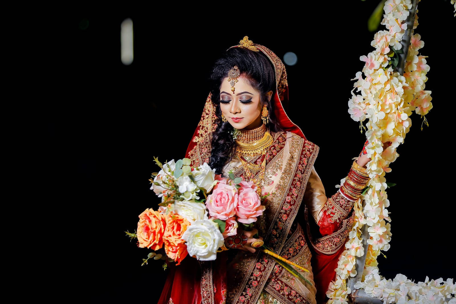 Indian 桌布 壁紙 — 一位身穿華麗紅金色傳統服飾、光彩照人的新娘，在深色背景下手持一束玫瑰。