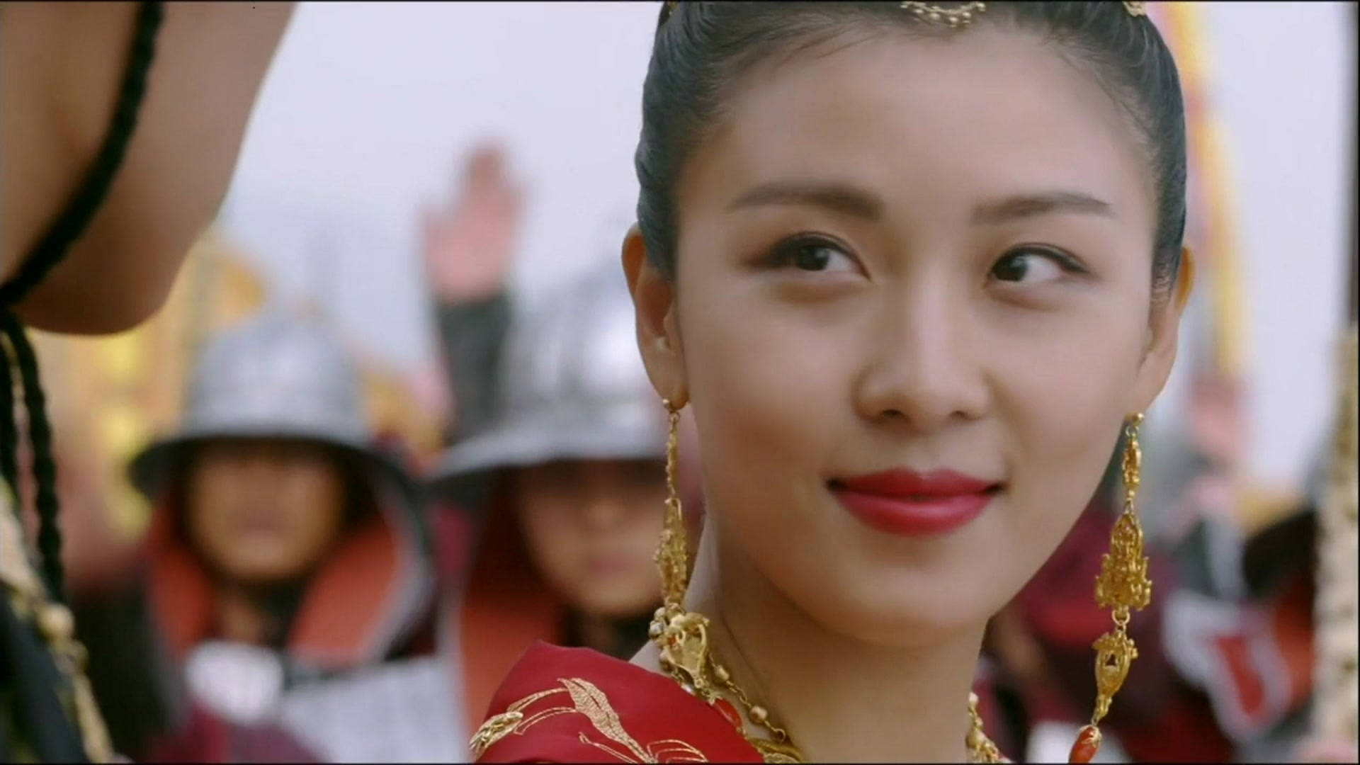 kdrama 桌布 壁紙 — 一位身穿華麗紅金色傳統服飾的女性，在模糊的盔甲人物背景下側視，帶著微妙的微笑。