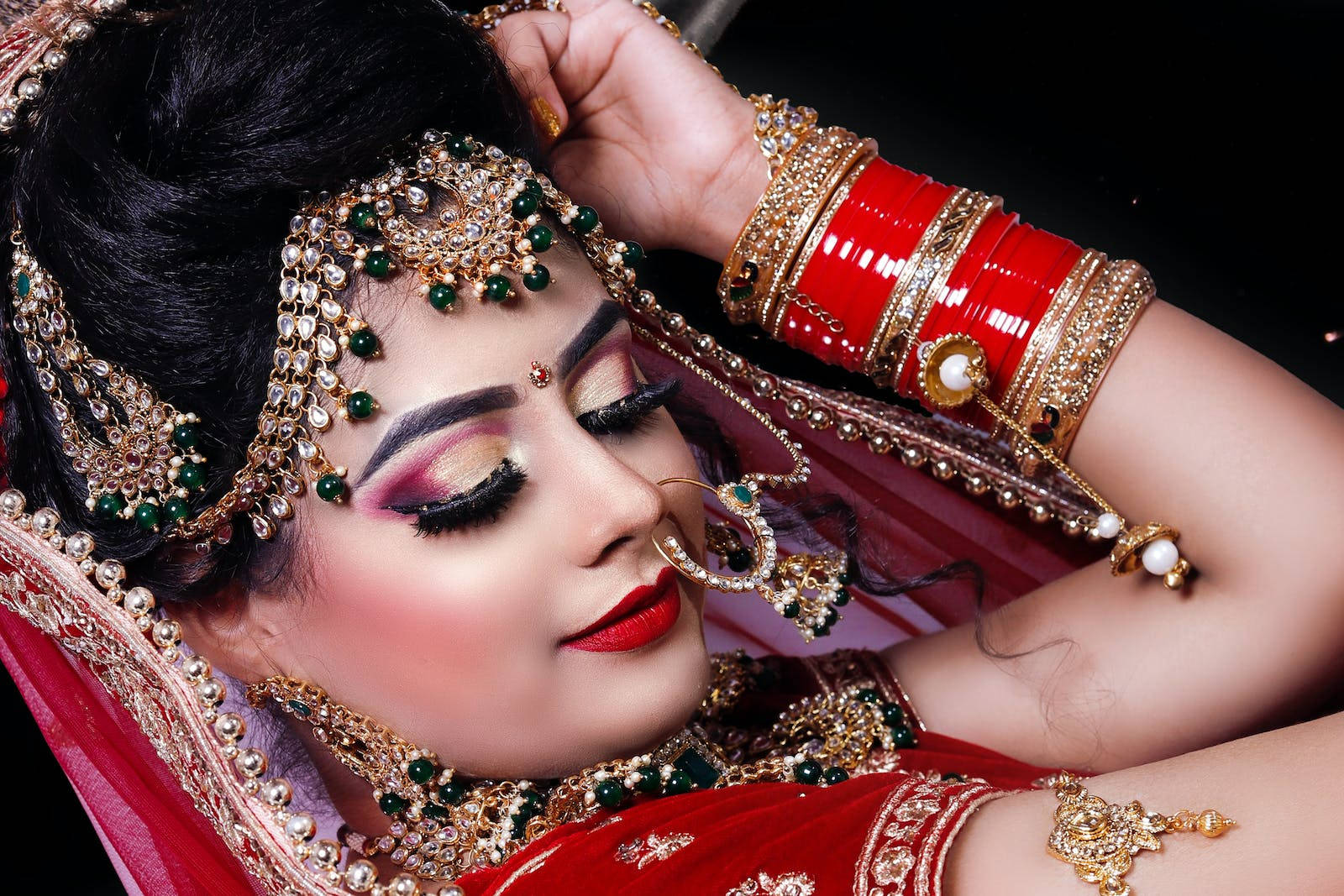 Indian 桌布 壁紙 — 一位身穿華麗紅金色新娘禮服、佩戴精緻珠寶和濃妝的女性，在深色背景下優雅地擺姿勢。