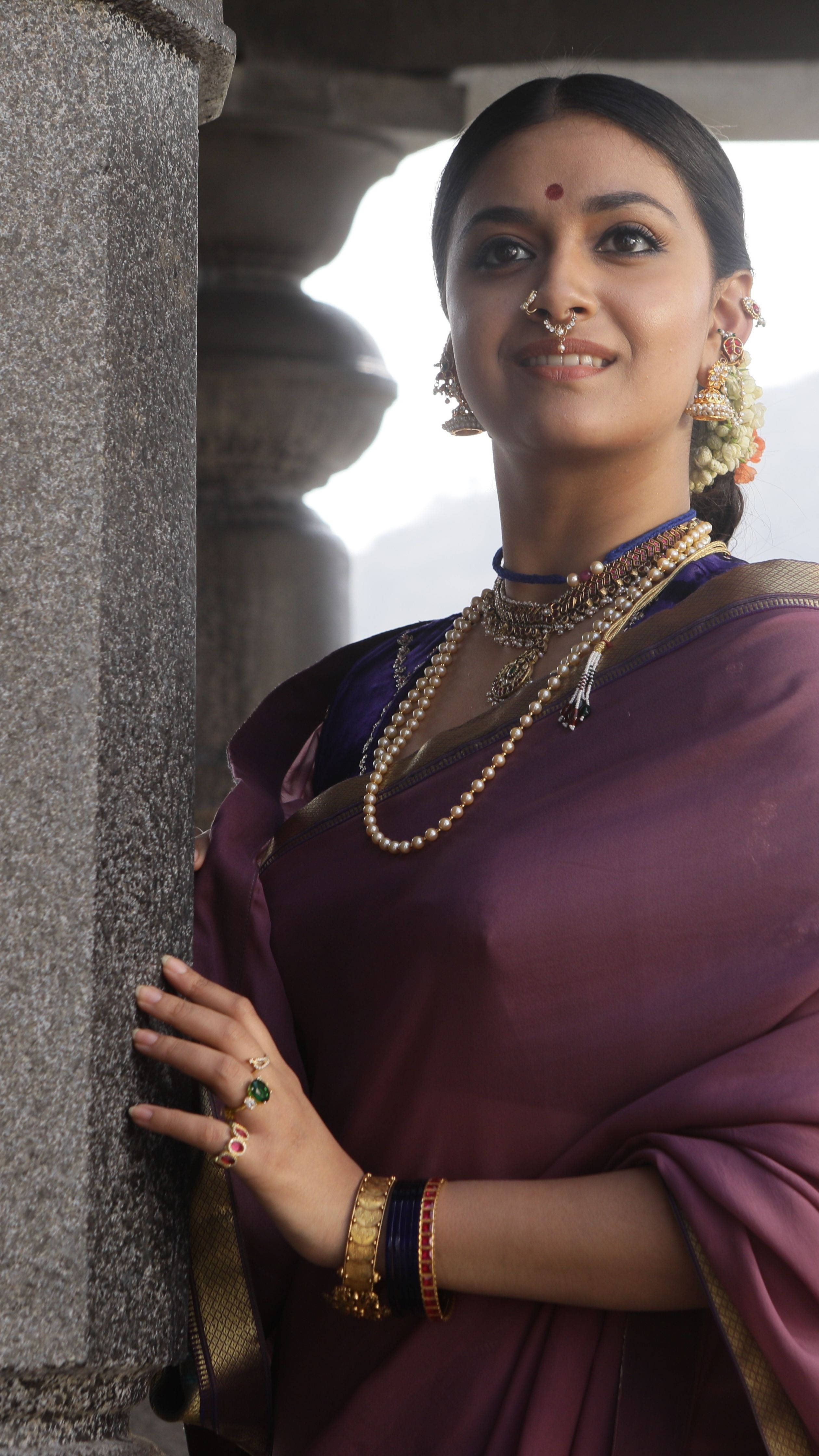 Indian 桌布 壁紙 — 一位身穿華麗紫色紗麗、佩戴黃金首飾的女子，在柔和日光下優雅地站在石柱旁。
