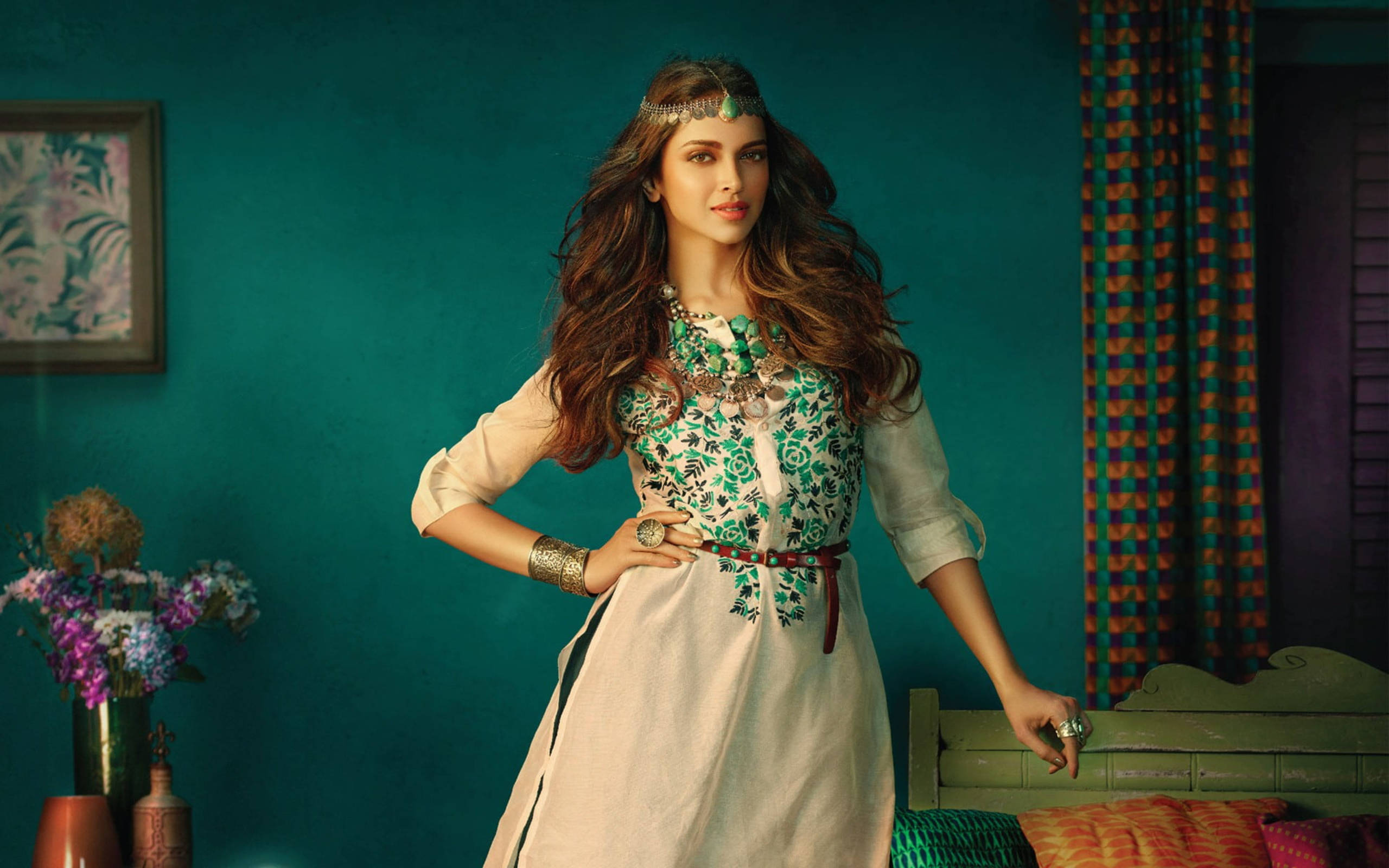 Deepika 桌布 壁紙 — 一位身穿華麗綠色刺繡服裝的女性，在裝飾豐富的藍綠色牆壁房間中自信地擺姿勢，房間內有圖案窗簾和花卉點綴。