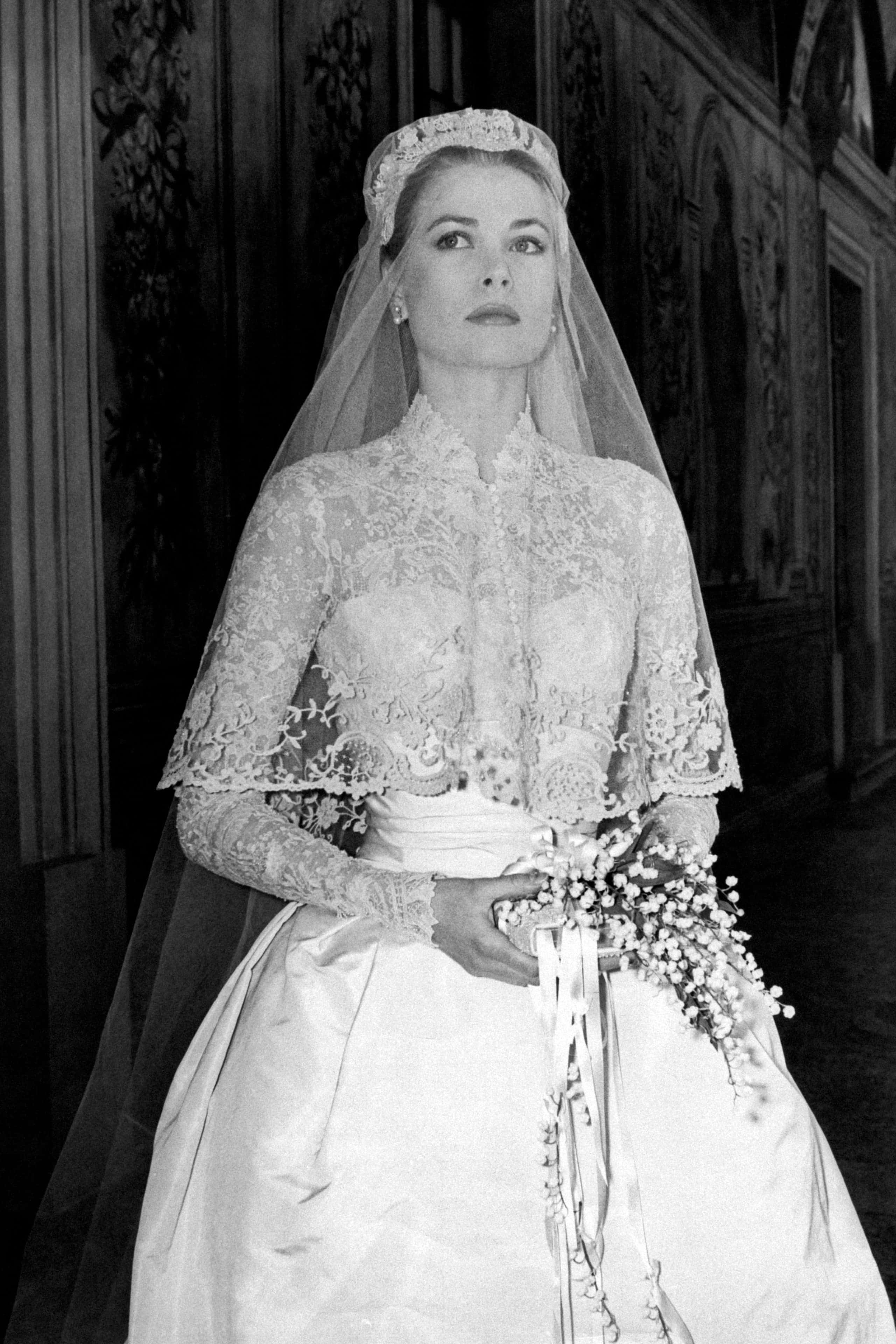 Black And White Wedding 桌布 壁紙 — 一位身穿華麗蕾絲婚紗和頭紗的新娘，在宏偉華麗的走廊裡手持花束。
