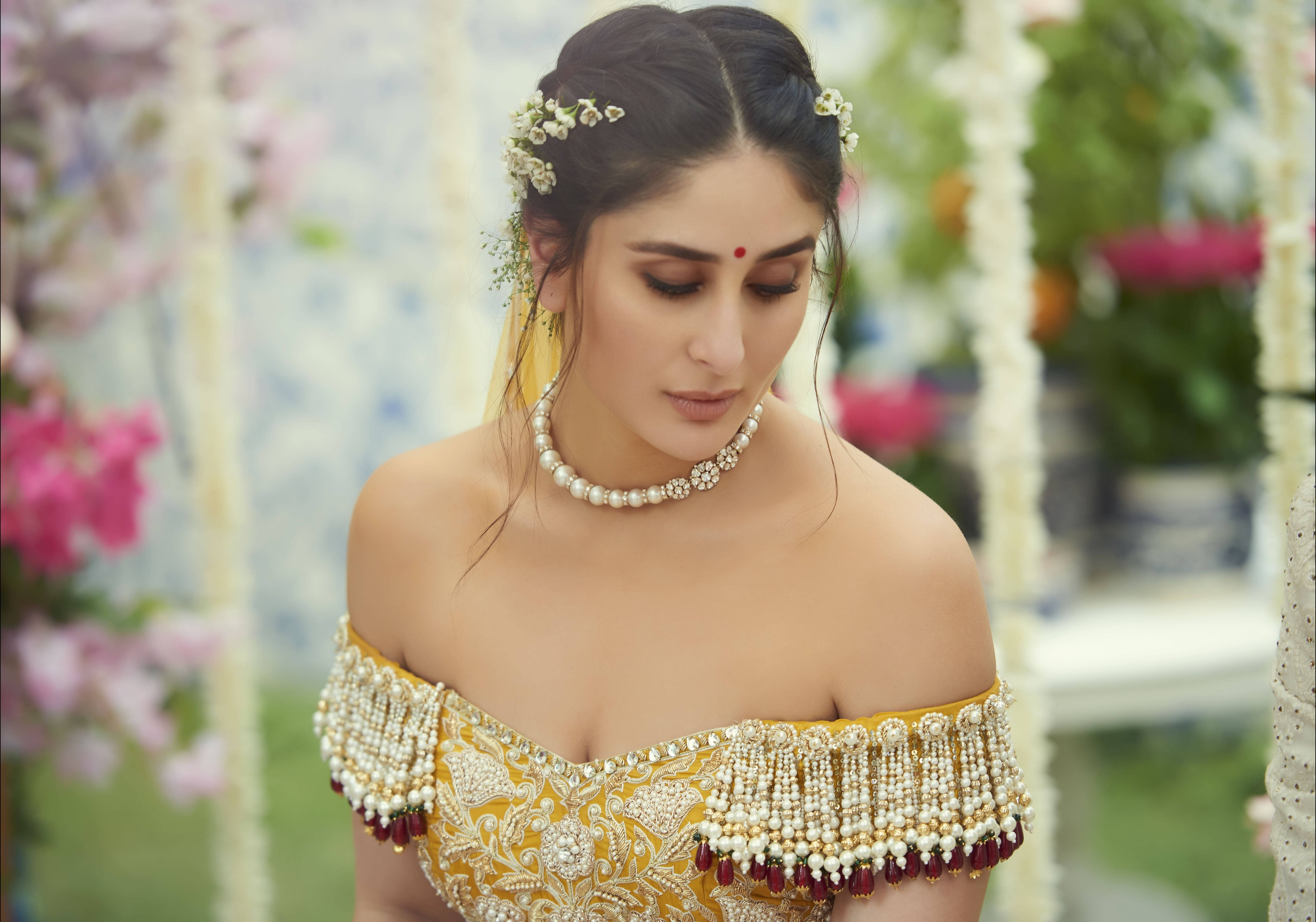 Kareena 桌布 壁紙 — 一位身穿華麗金色傳統服飾、飾有珍珠和花卉髮飾的女子，在柔和光線的花園環境中低頭凝視。