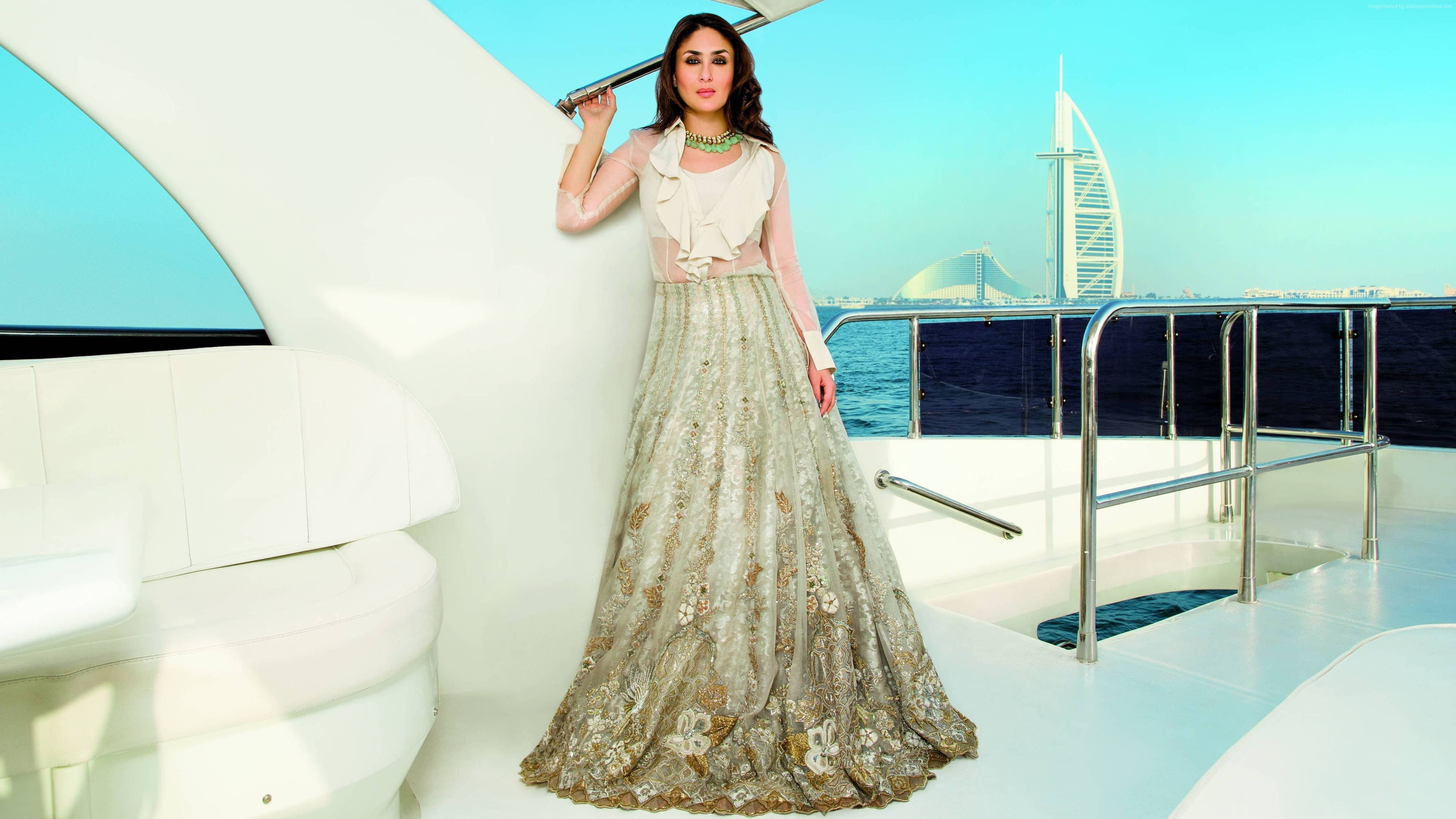 Kareena 桌布 壁紙 — 一位身穿華麗金色和奶油色長裙的女性優雅地站在豪華遊艇上，背景可見帆船酒店。