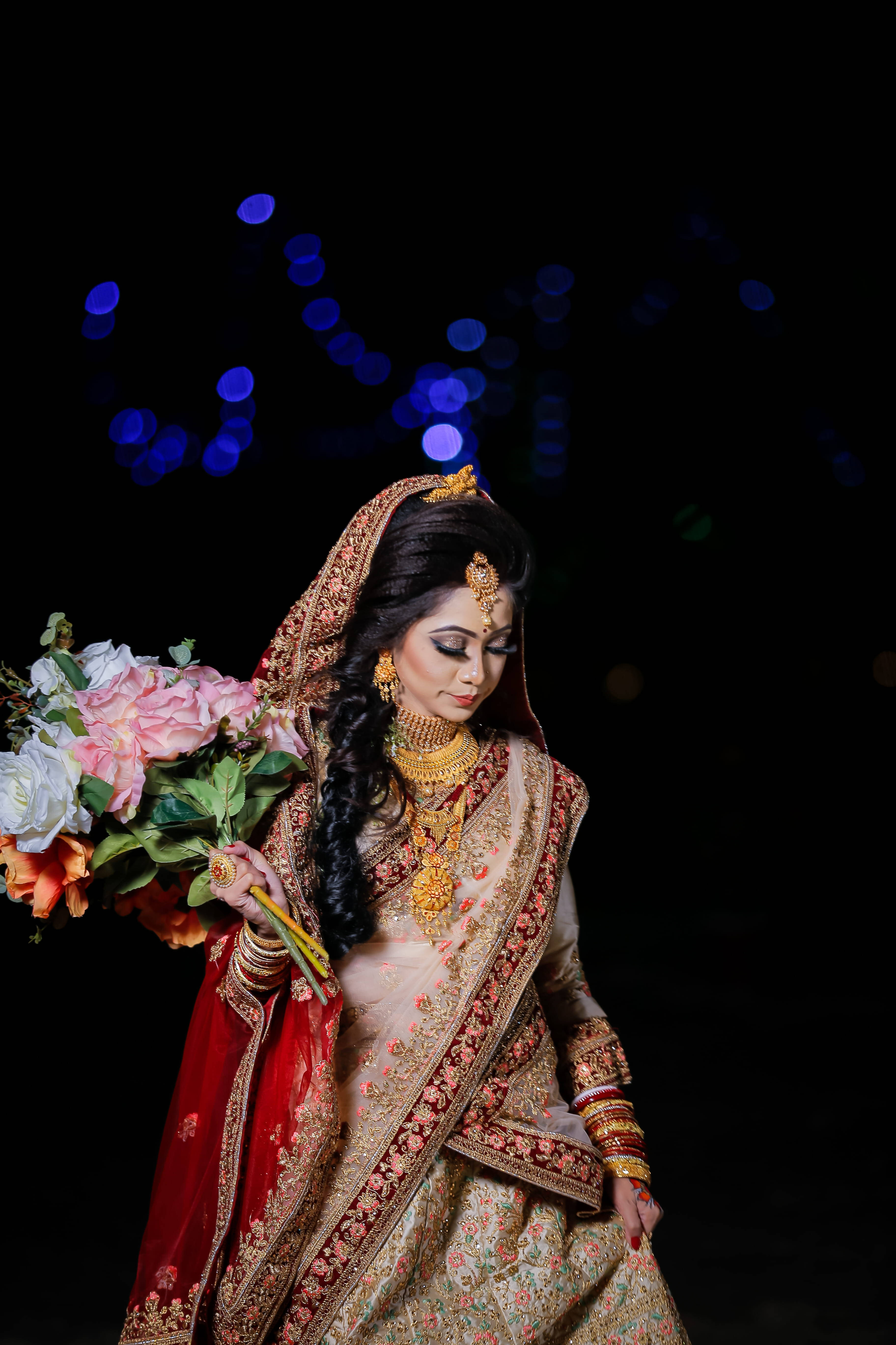 Wedding Dress 桌布 壁紙 — 一位身穿華麗金色和紅色傳統服飾的新娘，在帶有藍色散景燈光的黑暗背景下，手持色彩繽紛的花束。