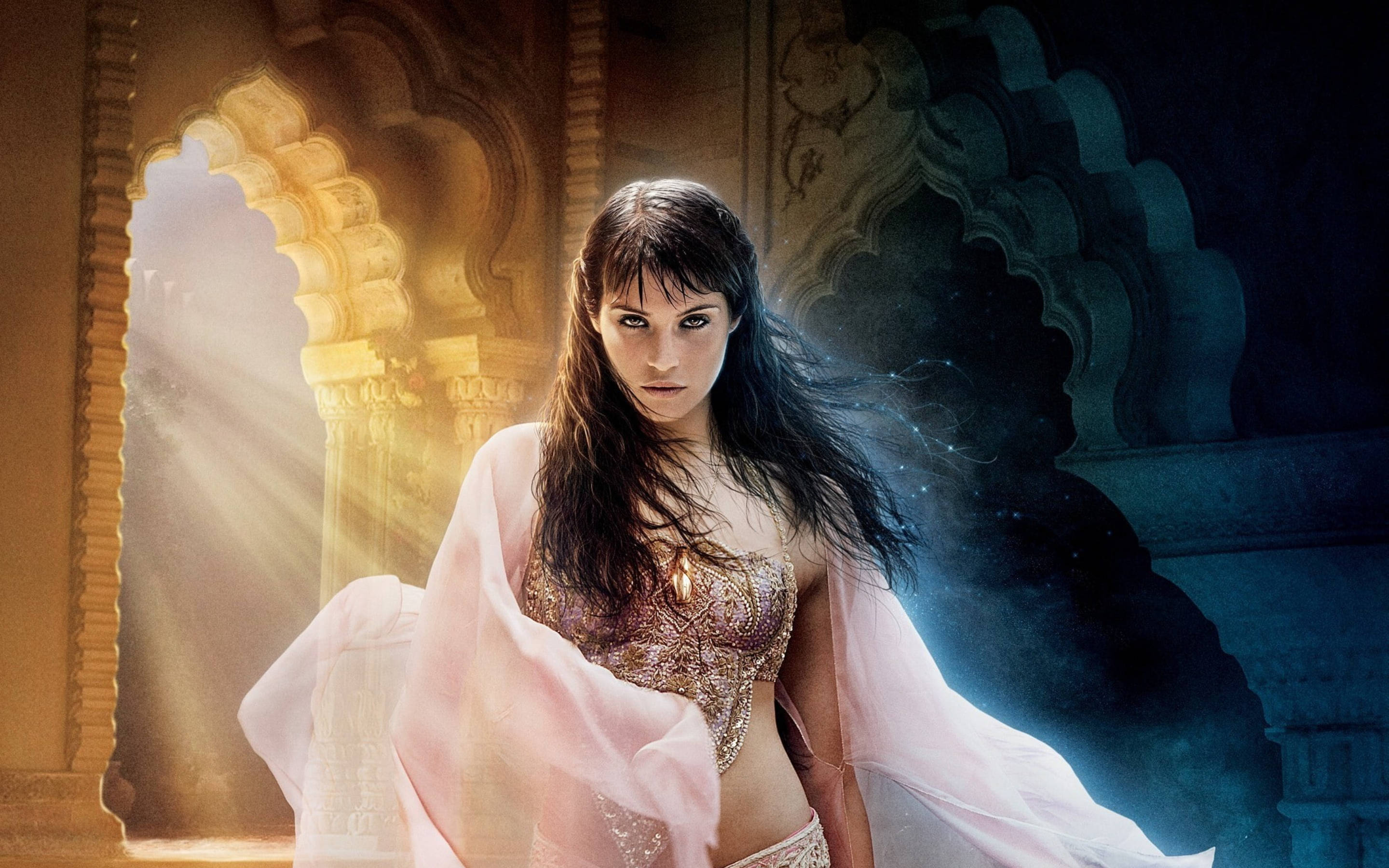 Gemma Arterton 桌布 壁紙 — 一位身穿華麗金色服飾和飄逸粉紅布料的女人，站在宏偉的拱門中，陽光從她身後照射進來。