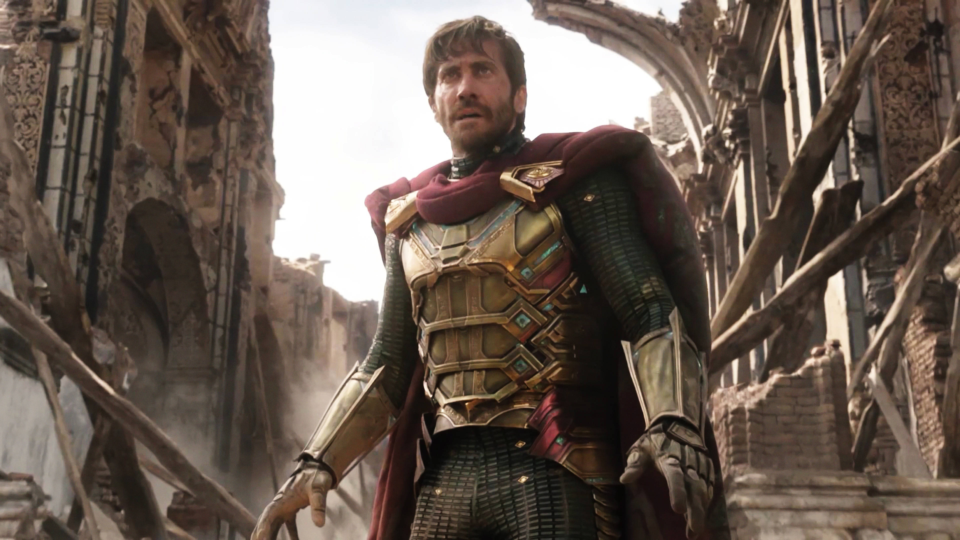 Mysterio 桌布 壁紙 — 一位身穿華麗金色盔甲和紅色斗篷的超級英雄，站在明亮的天空下，周圍是 crumbling 石頭廢墟。