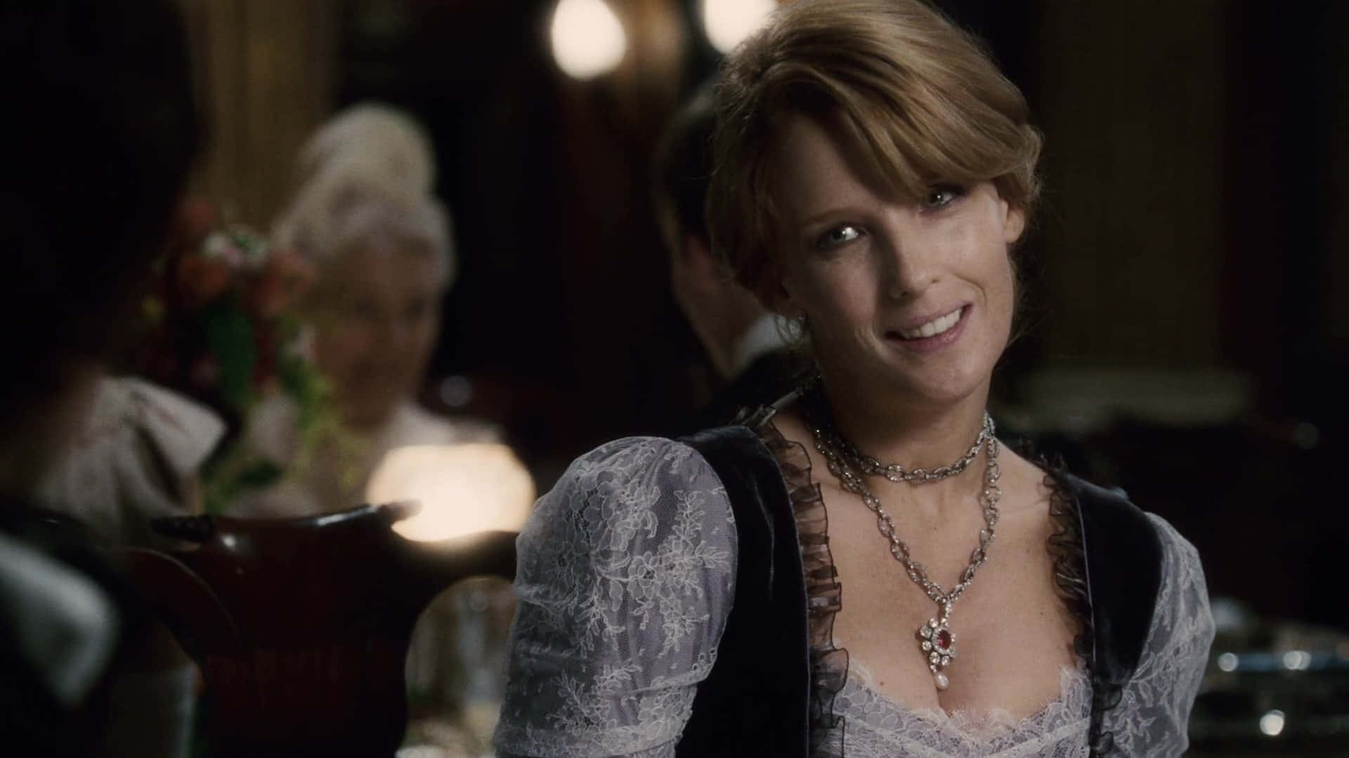 Kelly Reilly 桌布 壁紙 — 一位身穿蕾絲和天鵝絨的女性在昏暗的復古飯廳中，在柔和的燭光下溫暖地微笑。