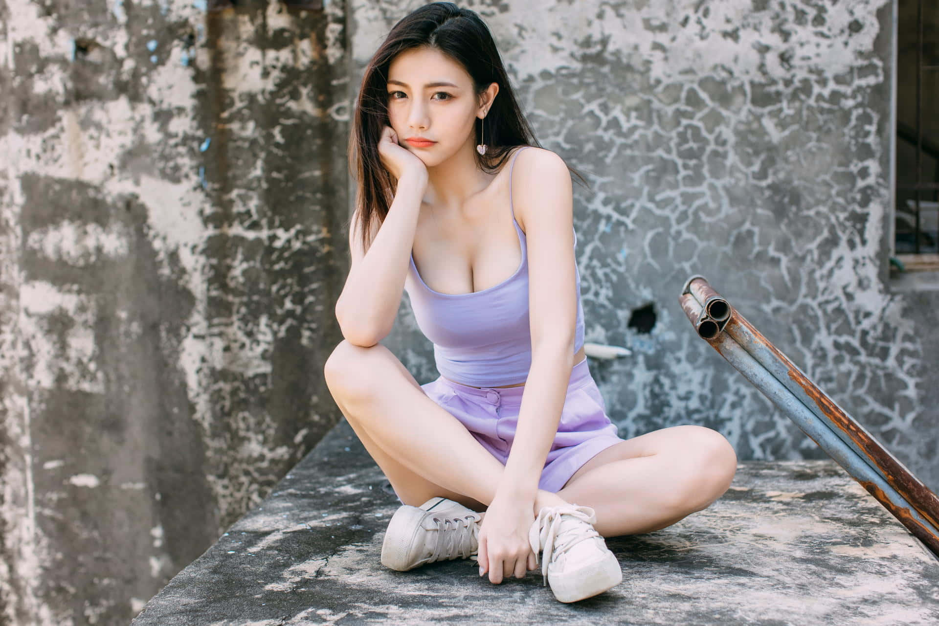 美女 桌布 壁紙 — 一位身穿薰衣草色服裝的年輕女性，靠著裂縫牆壁，若有所思地坐在風化的混凝土邊緣上。