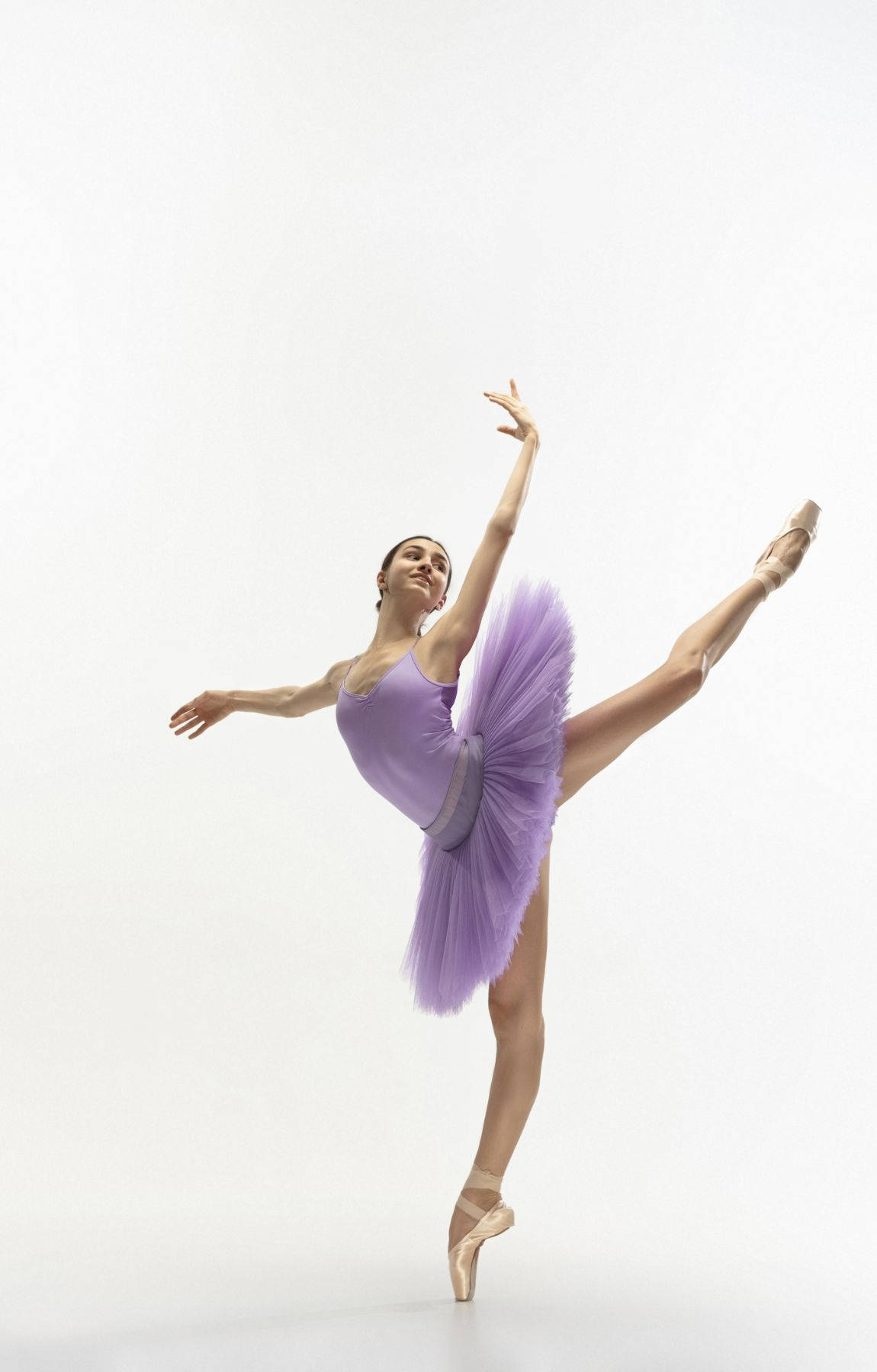 Ballet 桌布 壁紙 — 一位身穿薰衣草色芭蕾舞裙的芭蕾舞者，在純白背景前優雅地踮起腳尖，單腿高舉保持平衡。