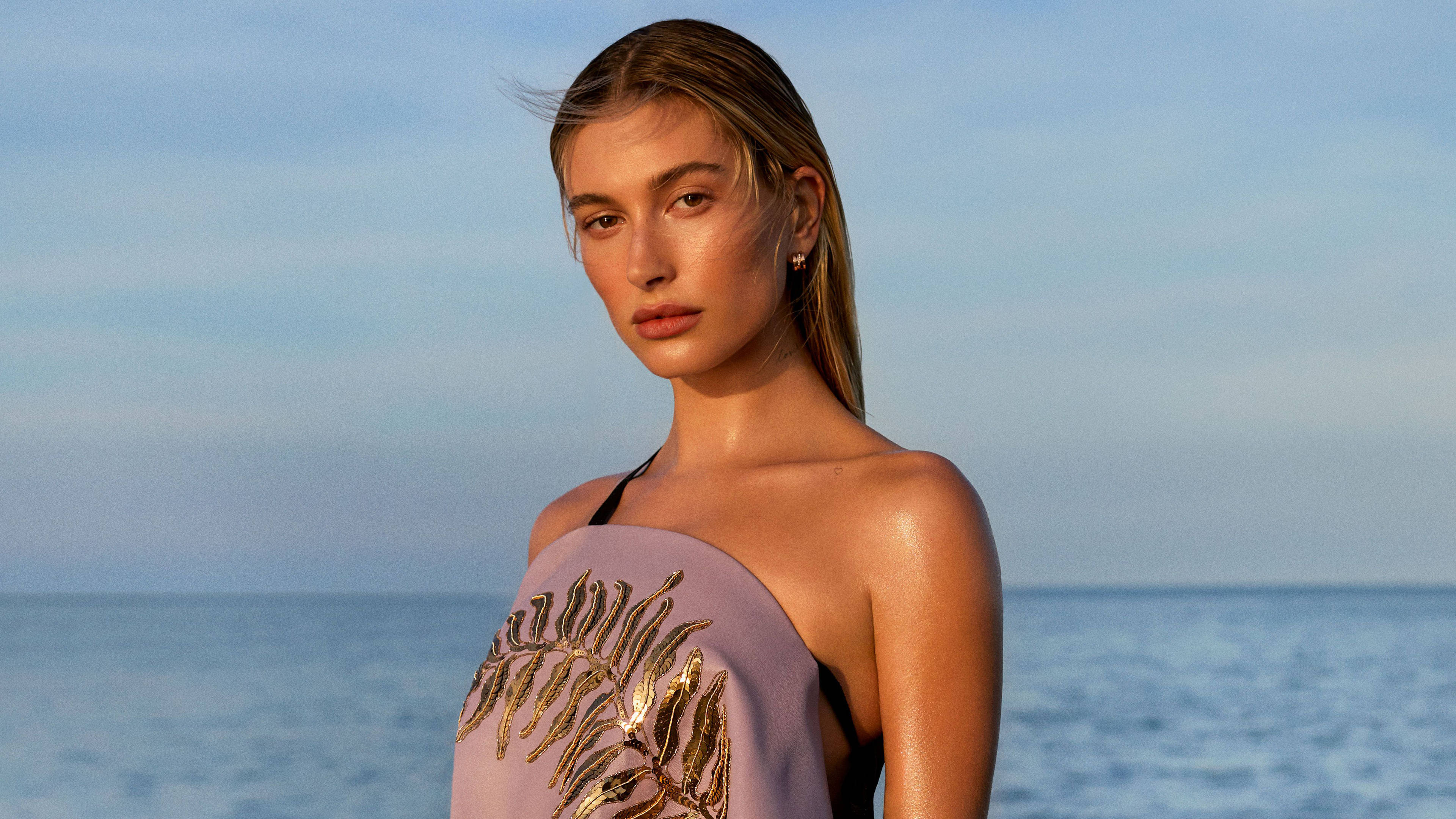 Hailey 桌布 壁紙 — 一位身穿薰衣草色葉子刺繡上衣的女性，在柔和的藍天下站在海邊。
