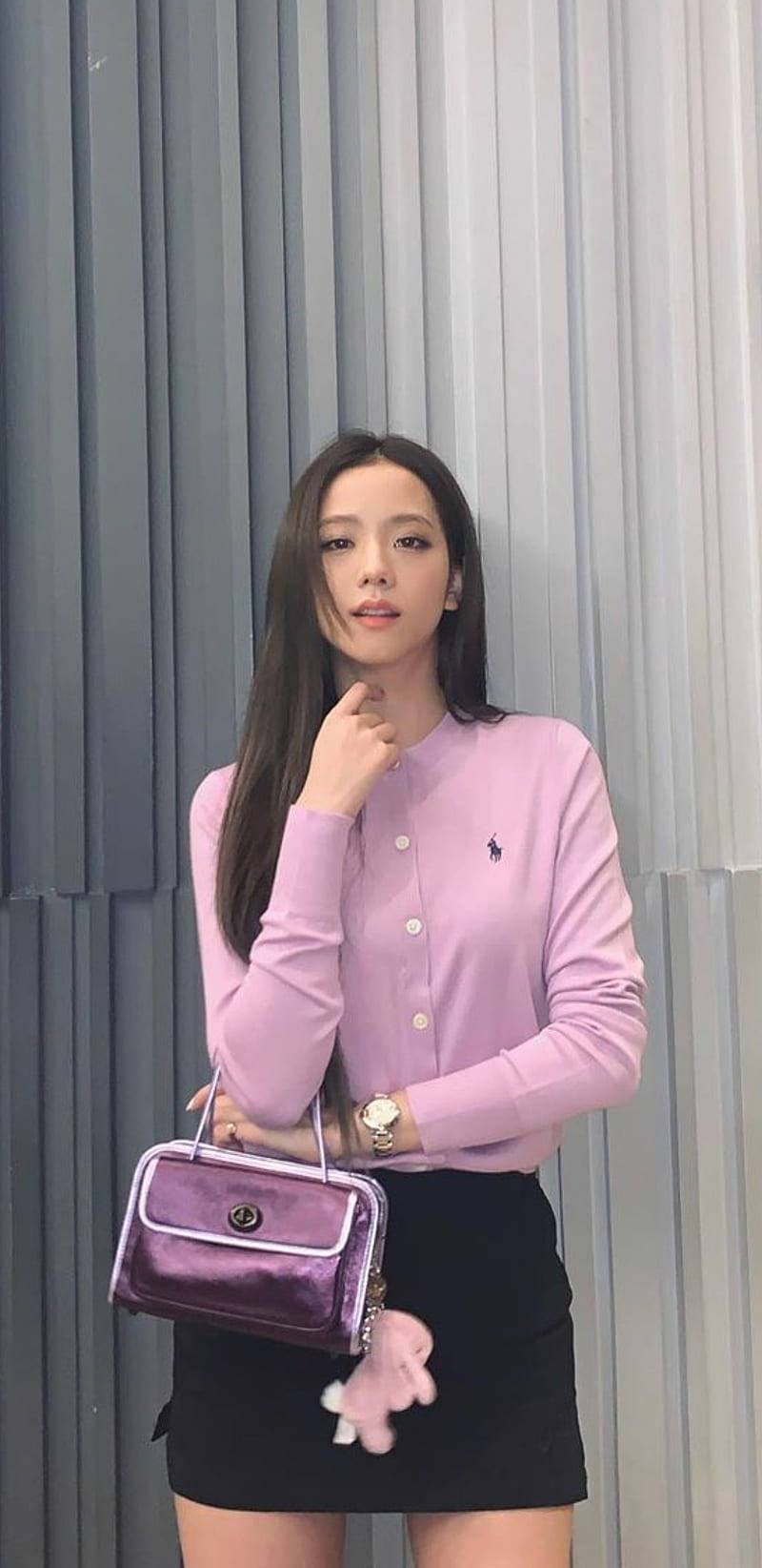 jisoo 可愛 桌布 壁紙 — 一位身穿薰衣草色鈕扣襯衫和黑色裙子的女士，拿著相配的紫色手袋，在灰色垂直百葉窗前擺姿勢。