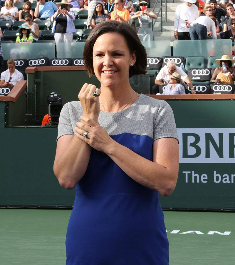 Tennis 桌布 壁紙 — 一位身穿藍灰色連衣裙的微笑女子在綠色網球場上慶祝，背景有觀眾。