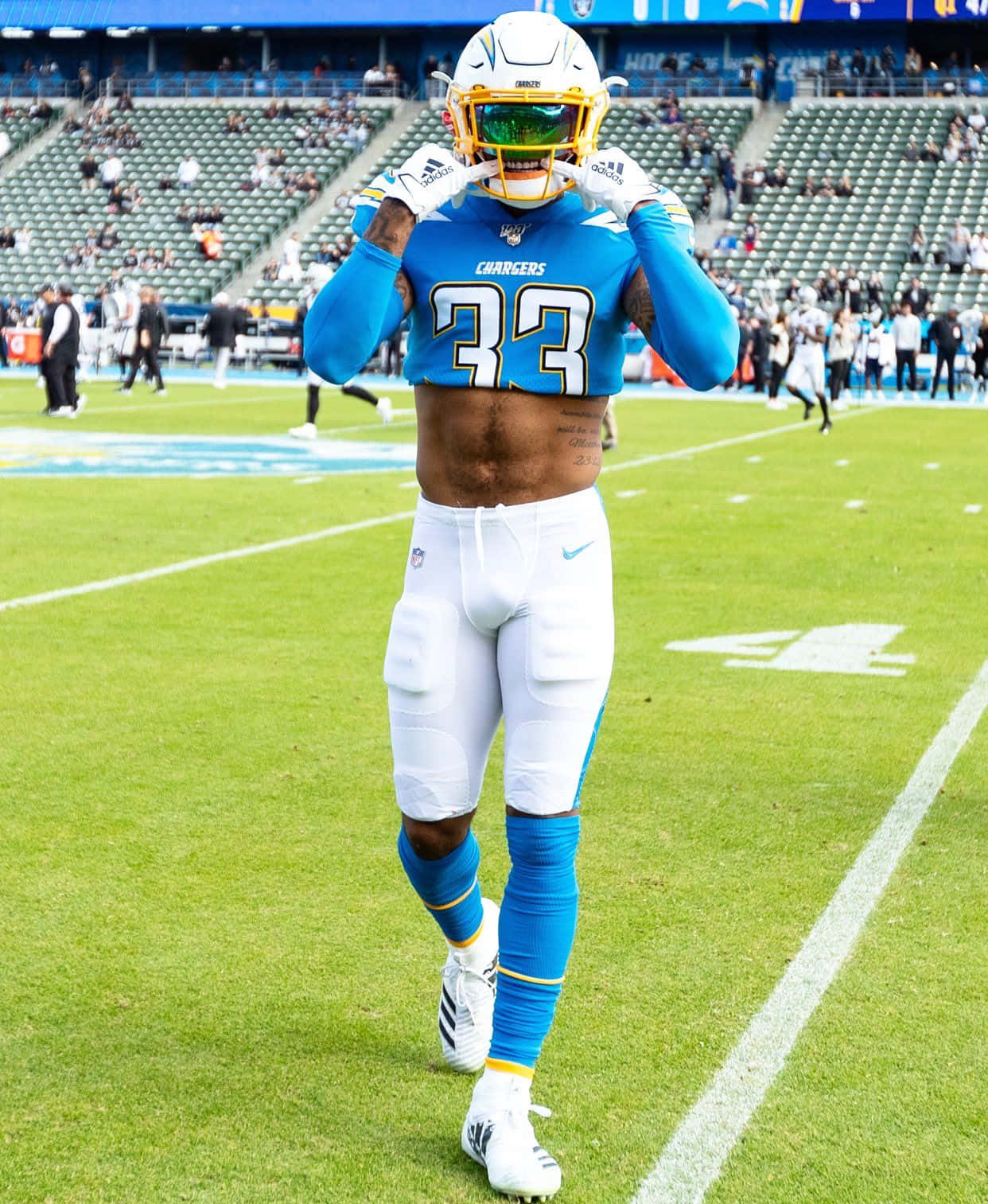 NFL 桌布 壁紙 — 一位身穿藍白球衣的 Chargers 美式足球員在陽光明媚的球場上調整頭盔。