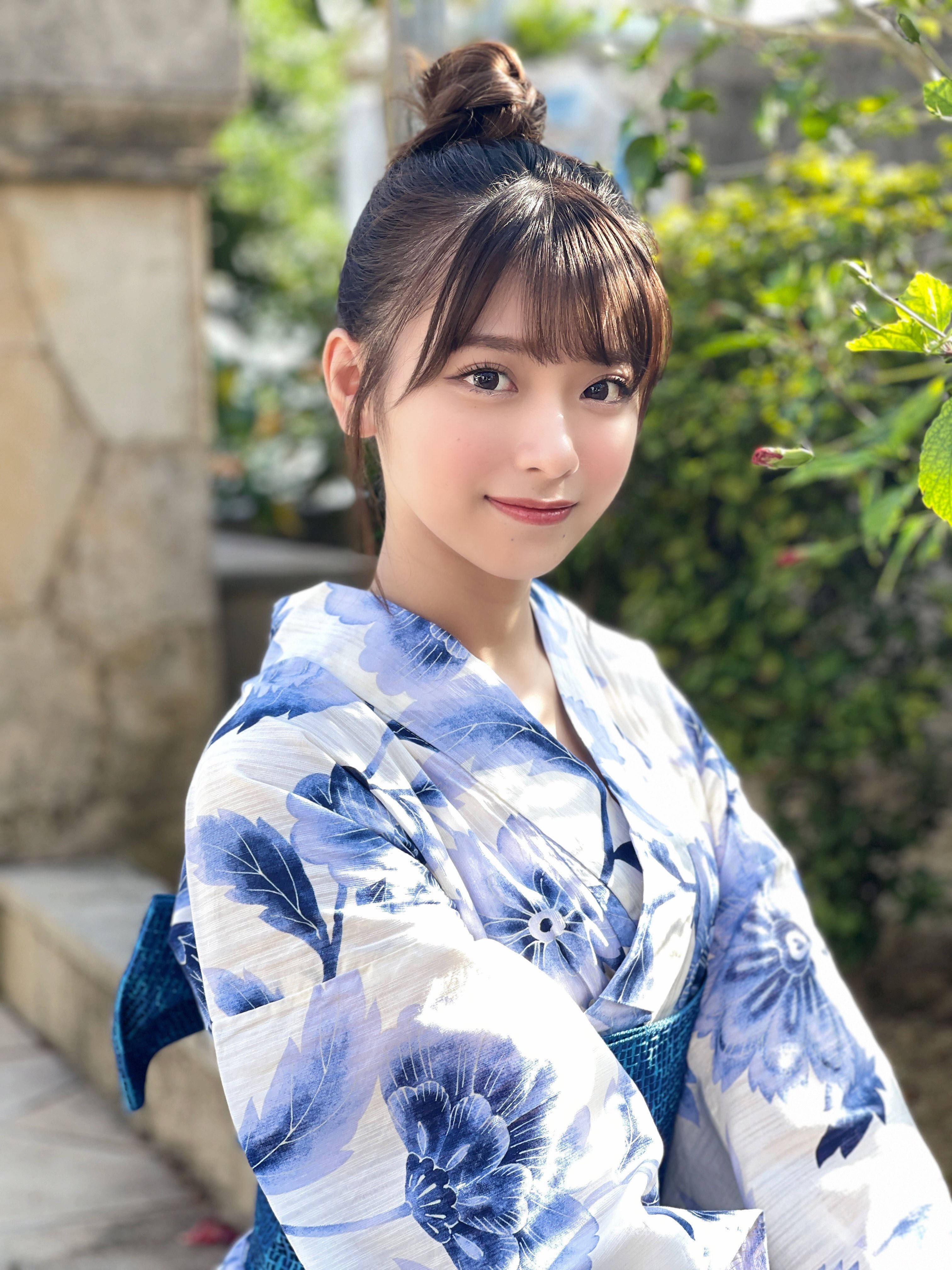 美女 桌布 壁紙 — 一位身穿藍白花卉和服的年輕女性在陽光普照的花園背景下，以石頭建築為襯，溫柔地微笑。