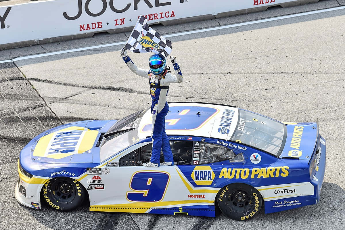 nascar 桌布 壁紙 — 一位身穿藍白裝備的NASCAR車手站在他的藍黃色9號賽車上，在賽道上揮舞著方格旗。