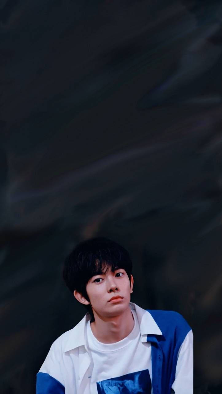 Kpop Aesthetic 桌布 壁紙 — 一位身穿藍白襯衫的年輕男子在深色紋理背景前若有所思地凝視。