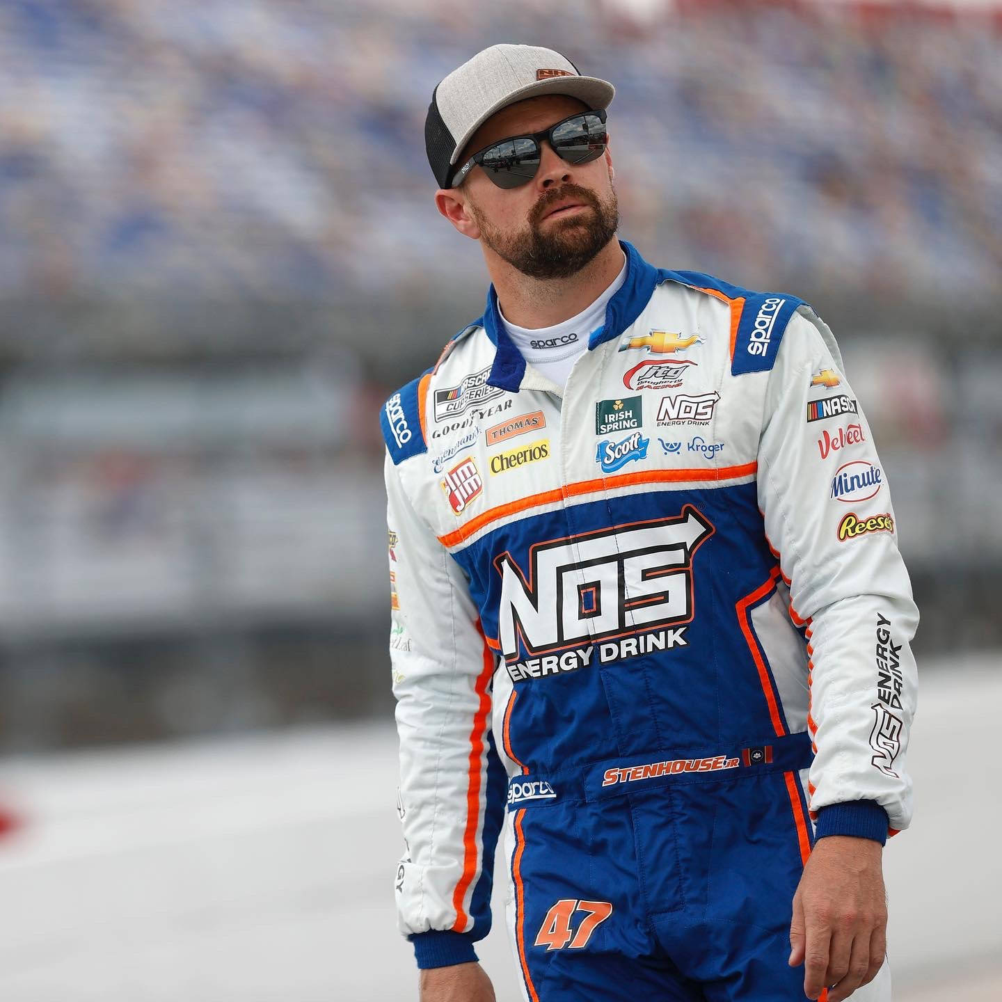 Athlete 桌布 壁紙 — 一位身穿藍白賽車服、帶有贊助商標誌的NASCAR車手站在賽道上，表情嚴肅地向上看。