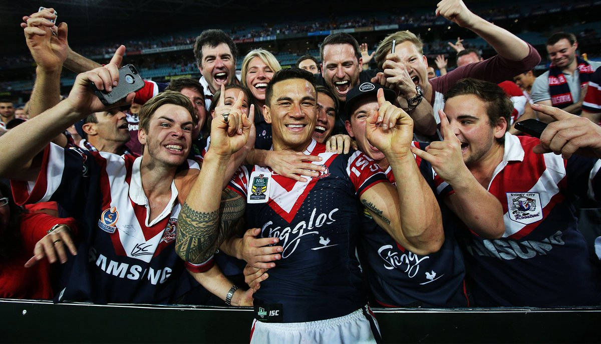 Nrl 桌布 壁紙 — 一位身穿藍紅球衣的歡欣橄欖球聯賽球員在體育場內被歡呼的隊友和球迷擁抱。