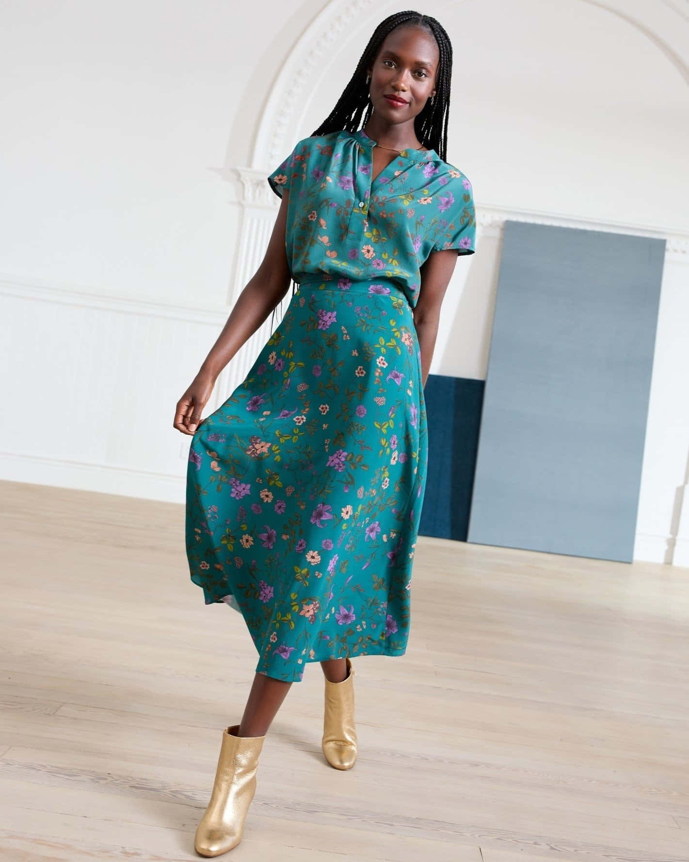 Beautiful Fashion 桌布 壁紙 — 一位身穿藍綠色花卉連衣裙和金色靴子的女性自信地站在一個光線充足的簡約房間裡，房間有白色牆壁和木地板。