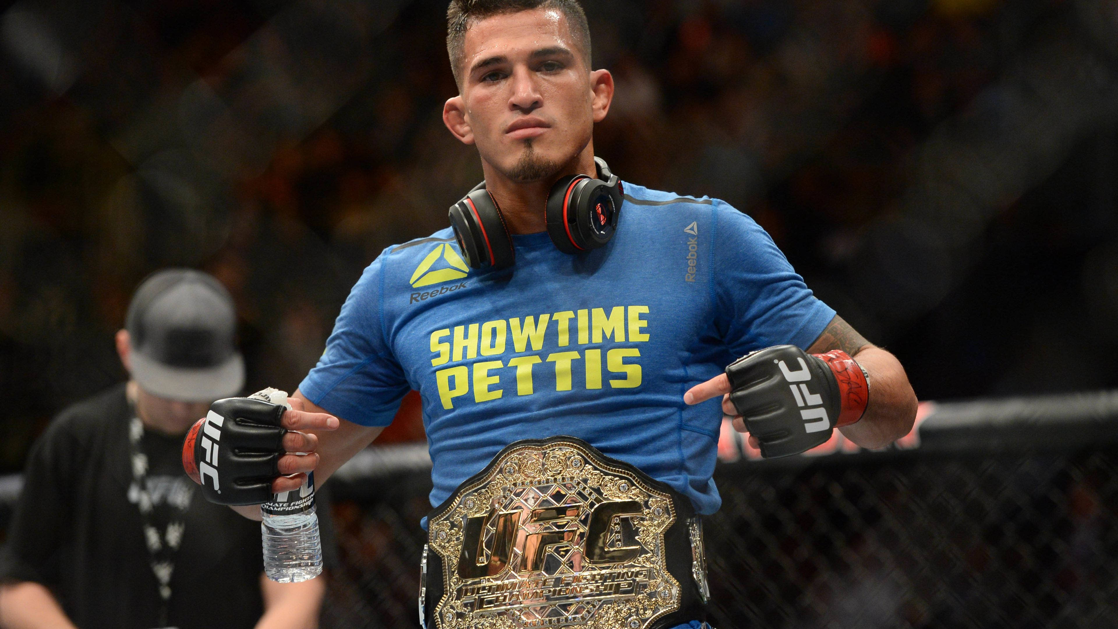 UFC 桌布 壁紙 — 一位身穿藍色「Showtime Pettis」T恤的勝利UFC拳手，在八角籠內自豪地展示他的冠軍腰帶。