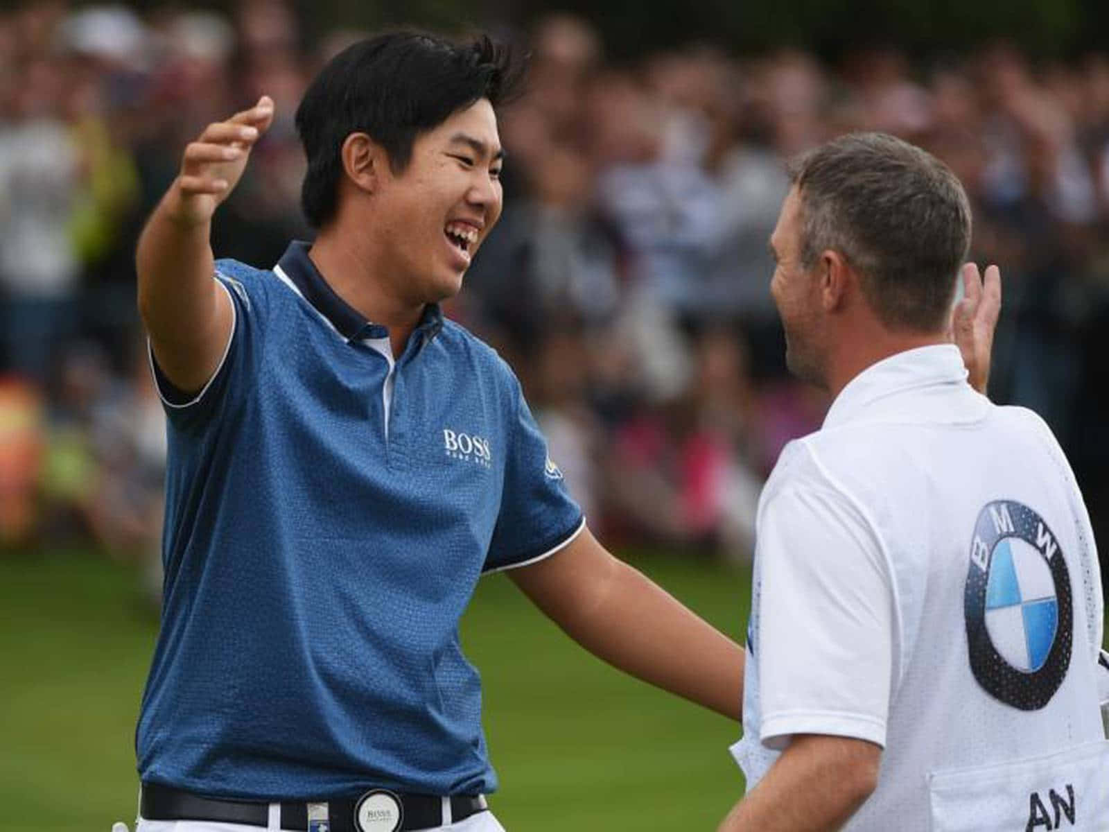 Champion 桌布 壁紙 — 一位身穿藍色Polo衫的快樂高爾夫球手，與一位身穿白色BMW襯衫的男子在綠色高爾夫球場上擊掌，背景有模糊的觀眾。