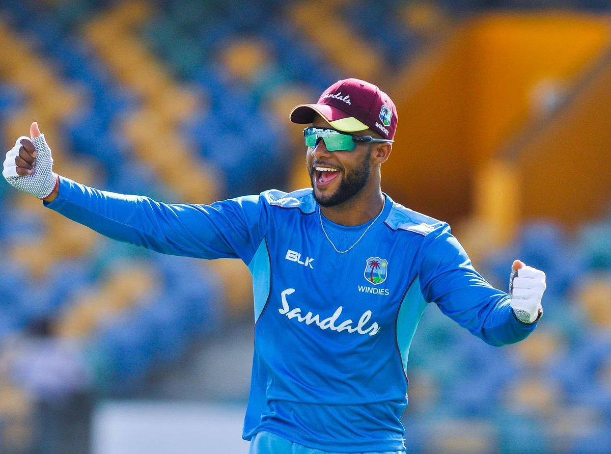 hope 桌布 壁紙 — 一位身穿藍色Windies球衣的快樂板球運動員在體育場燈光下張開雙臂，露出燦爛笑容慶祝。