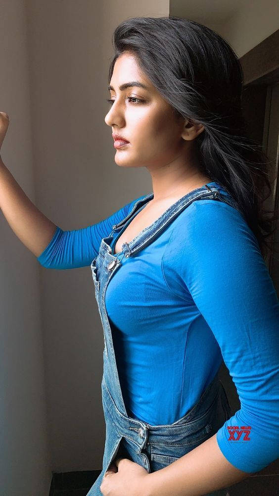 Bhojpuri 桌布 壁紙 — 一位身穿藍色上衣和牛仔吊帶褲的女性站在窗邊，陽光凸顯了她的側影和深色頭髮。