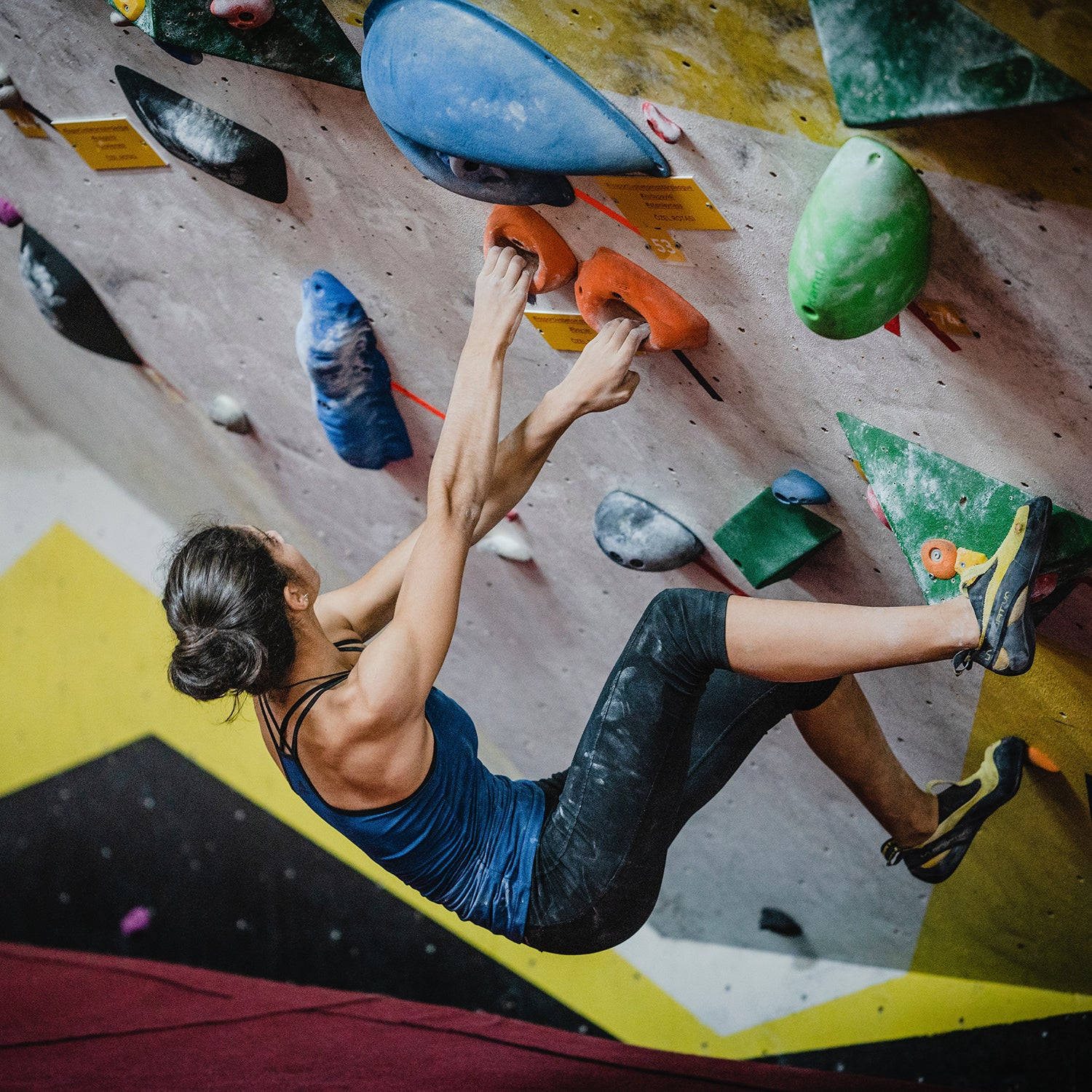 Climbing 桌布 壁紙 — 一位身穿藍色上衣的女性攀岩者，以專注的決心攀爬色彩繽紛的室內攀岩牆。