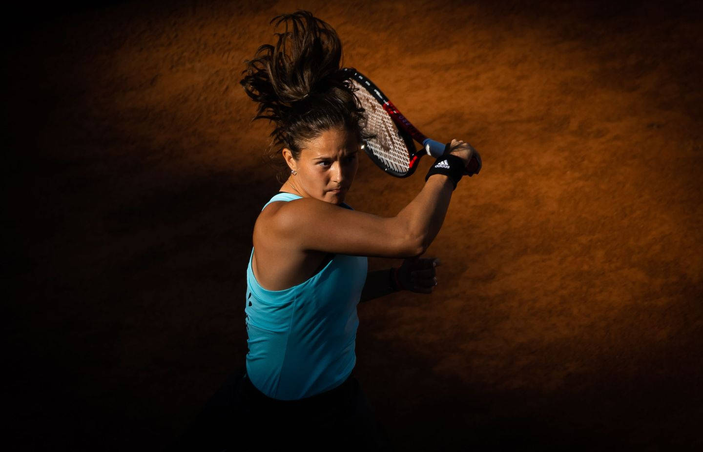 Athletic 桌布 壁紙 — 一位身穿藍色上衣的女網球運動員在戲劇性燈光下，在紅土場上專注地揮拍。
