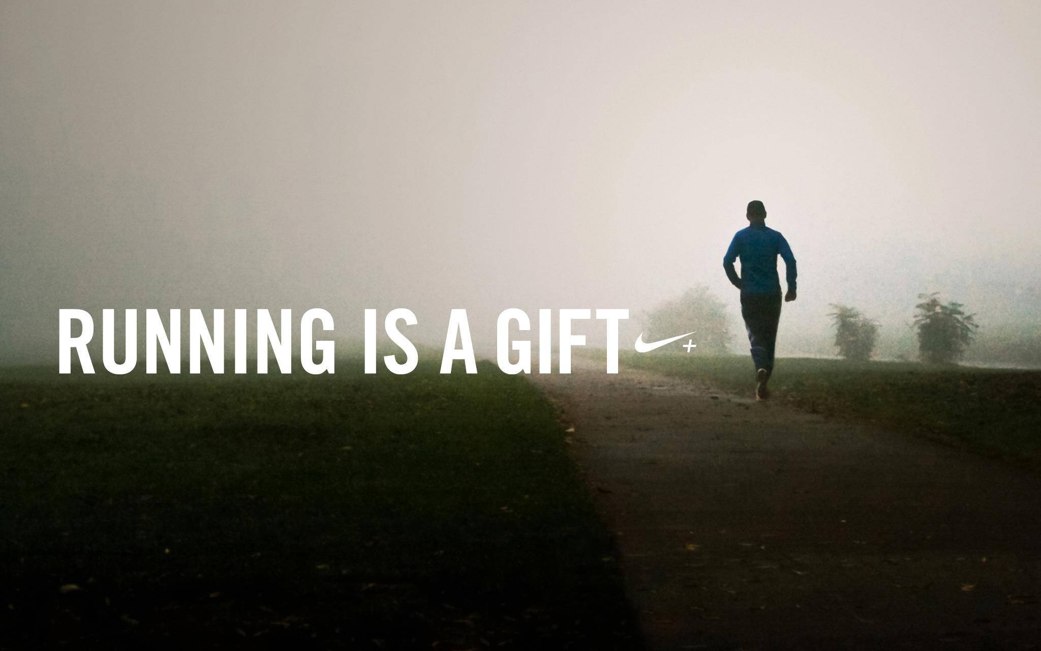 Marathon 桌布 壁紙 — 一位身穿藍色上衣的孤獨跑者，在黎明時分沿著一條霧濛濛的小徑穿過霧濛濛的公園，上面覆蓋著文字 running is a gift。
