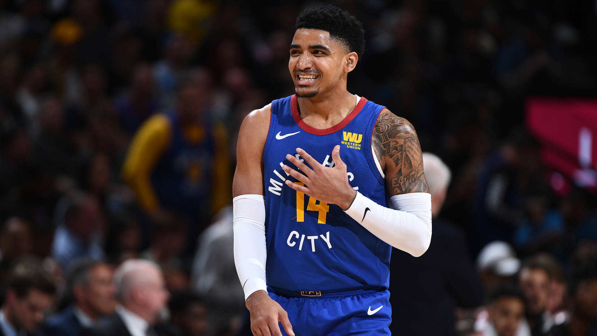 gary harris 桌布 壁紙 — 一位身穿藍色丹佛金塊隊球衣的籃球運動員在場館燈光下比賽時，手放在胸前微笑。