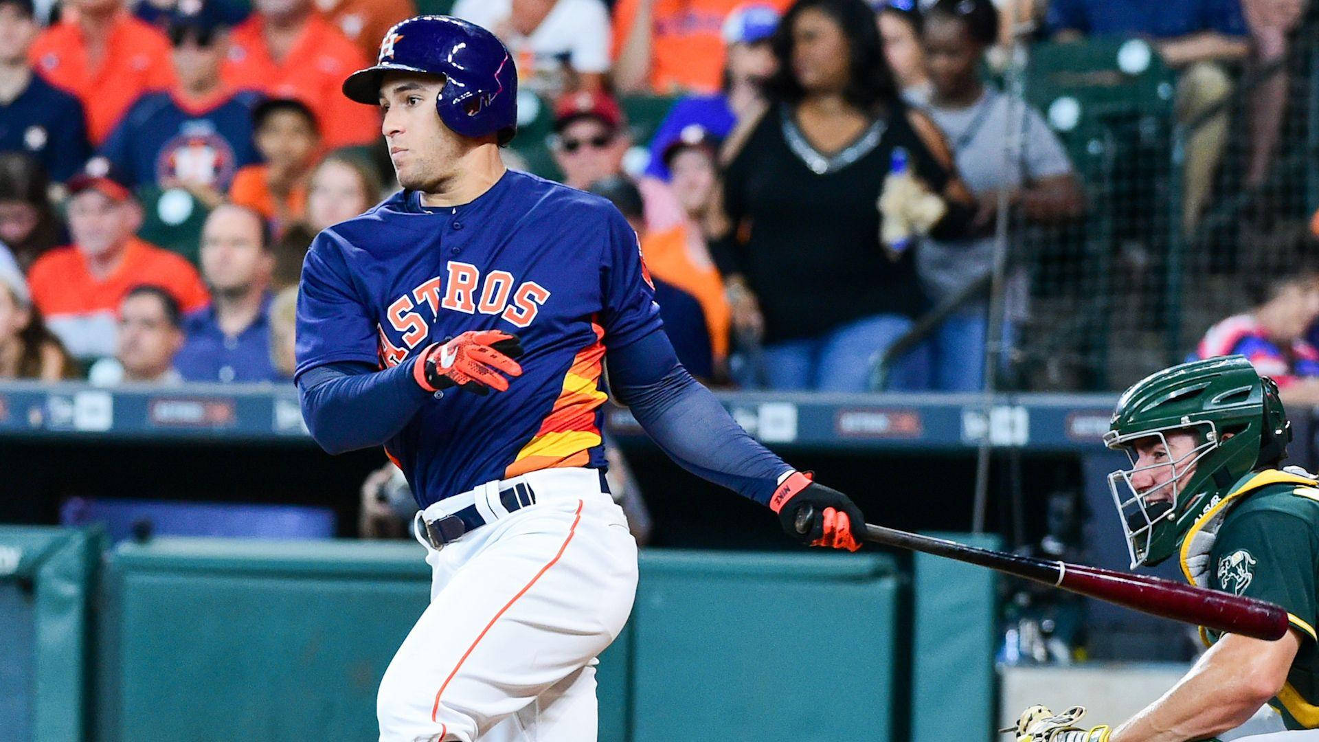 Bregman 桌布 壁紙 — 一位身穿藍色和橙色球衣的休士頓太空人棒球手在夜間比賽中揮棒，背景有捕手和人群。
