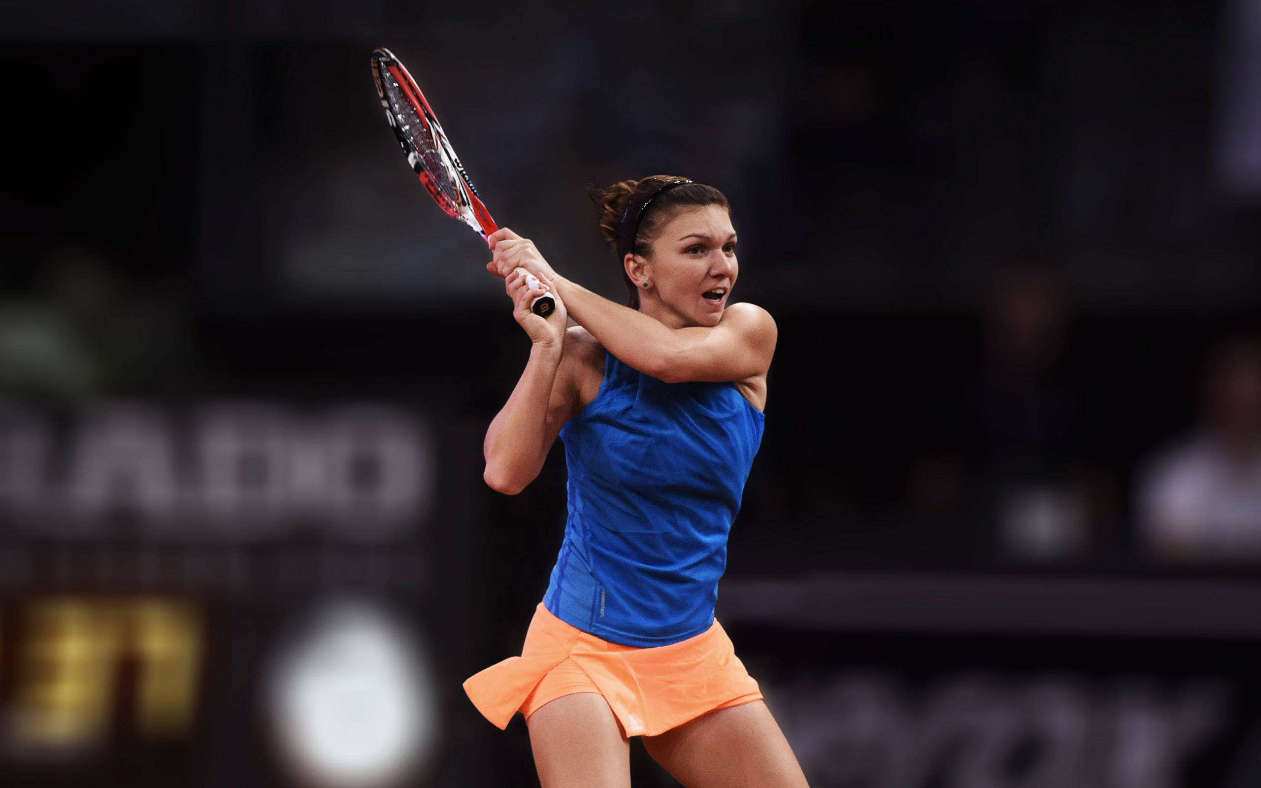 Tennis 桌布 壁紙 — 一位身穿藍色和橙色球衣的女網球選手在夜間比賽中專注地揮拍。