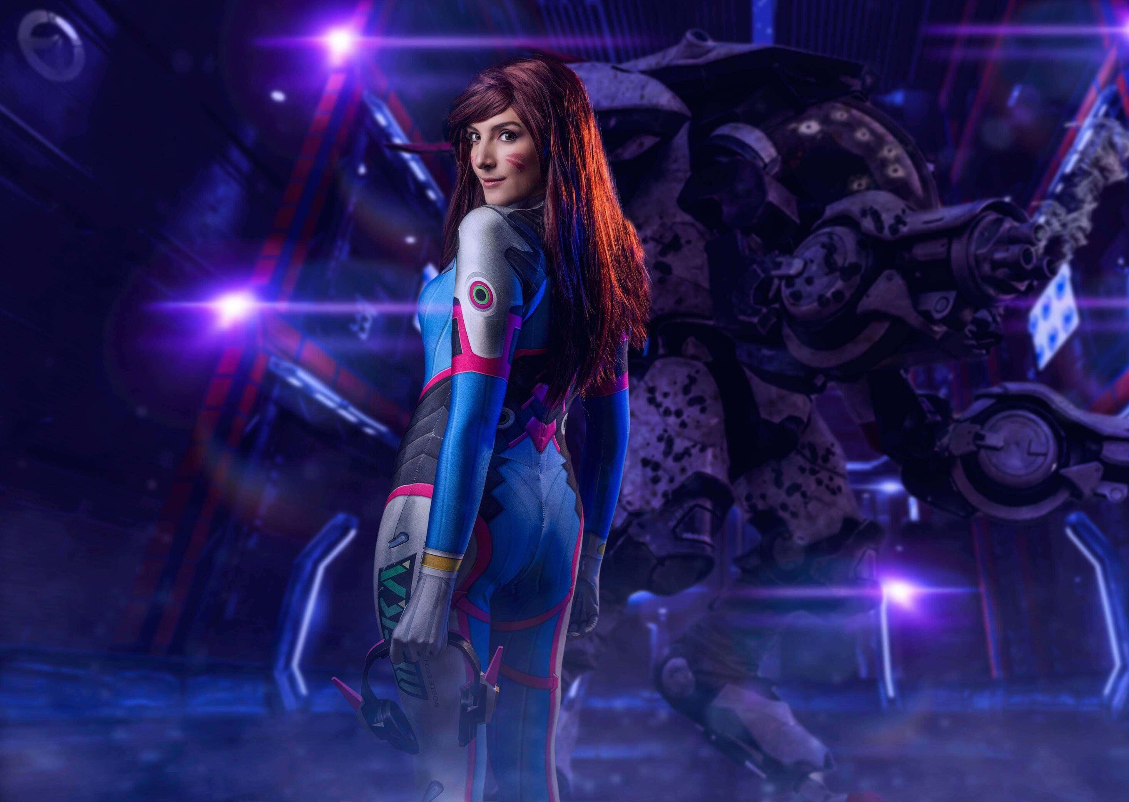 Gaming Cosplay 桌布 壁紙 — 一位身穿藍色和粉紅色未來風格套裝的女飛行員自信地站在一個巨大的機械機器人旁邊，周圍是發光的紫色燈光。