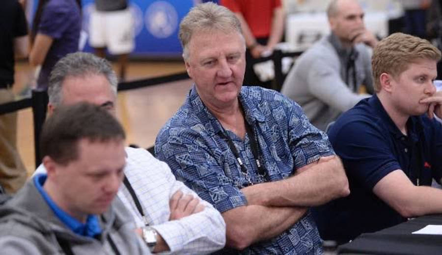 larry bird 桌布 壁紙 — 一位身穿藍色圖案襯衫的中年男子交叉雙臂坐著，觀看擁擠的室內場館中的活動。