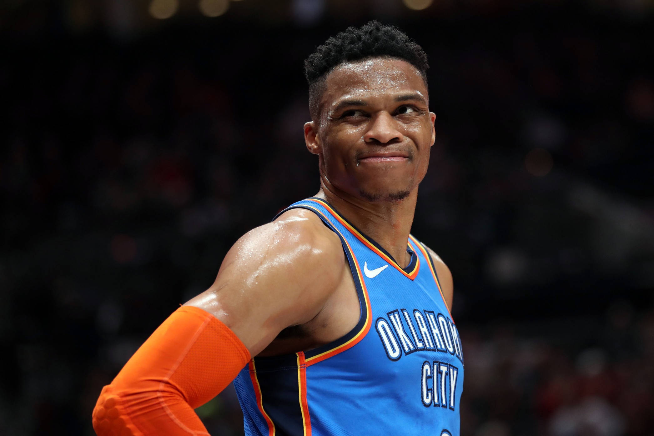Westbrook 桌布 壁紙 — 一位身穿藍色奧克拉荷馬城球衣的籃球運動員在比賽中自信地微笑，汗水在皮膚上閃閃發光。