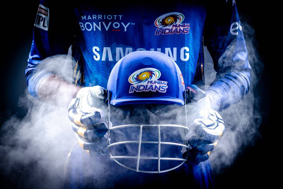Mumbai Indians 桌布 壁紙 — 一位身穿藍色孟買印第安人隊裝備的板球運動員在黑暗背景中旋轉的煙霧中手持頭盔。