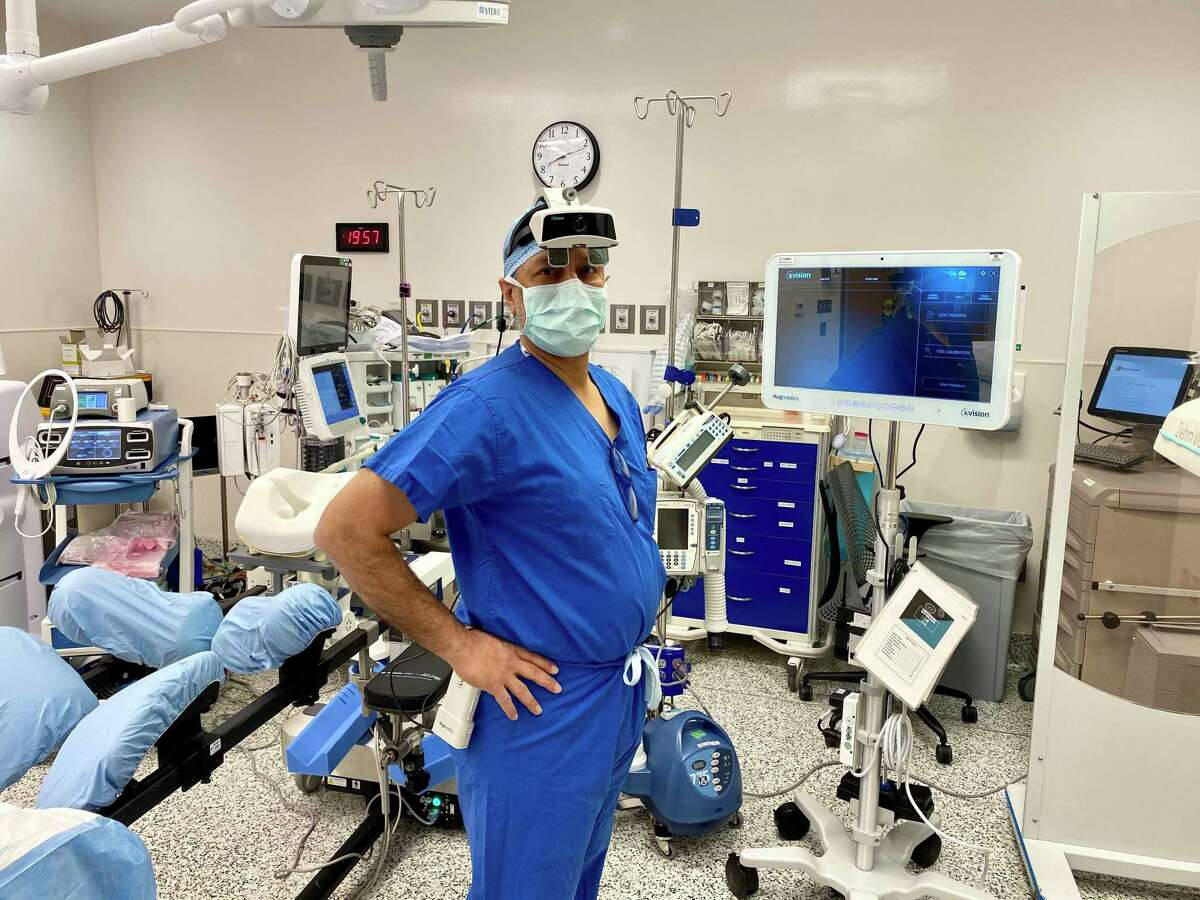 Surgeon 桌布 壁紙 — 一位身穿藍色手術服和口罩的外科醫生自信地站在高科技手術室中，周圍是醫療監視器和設備。