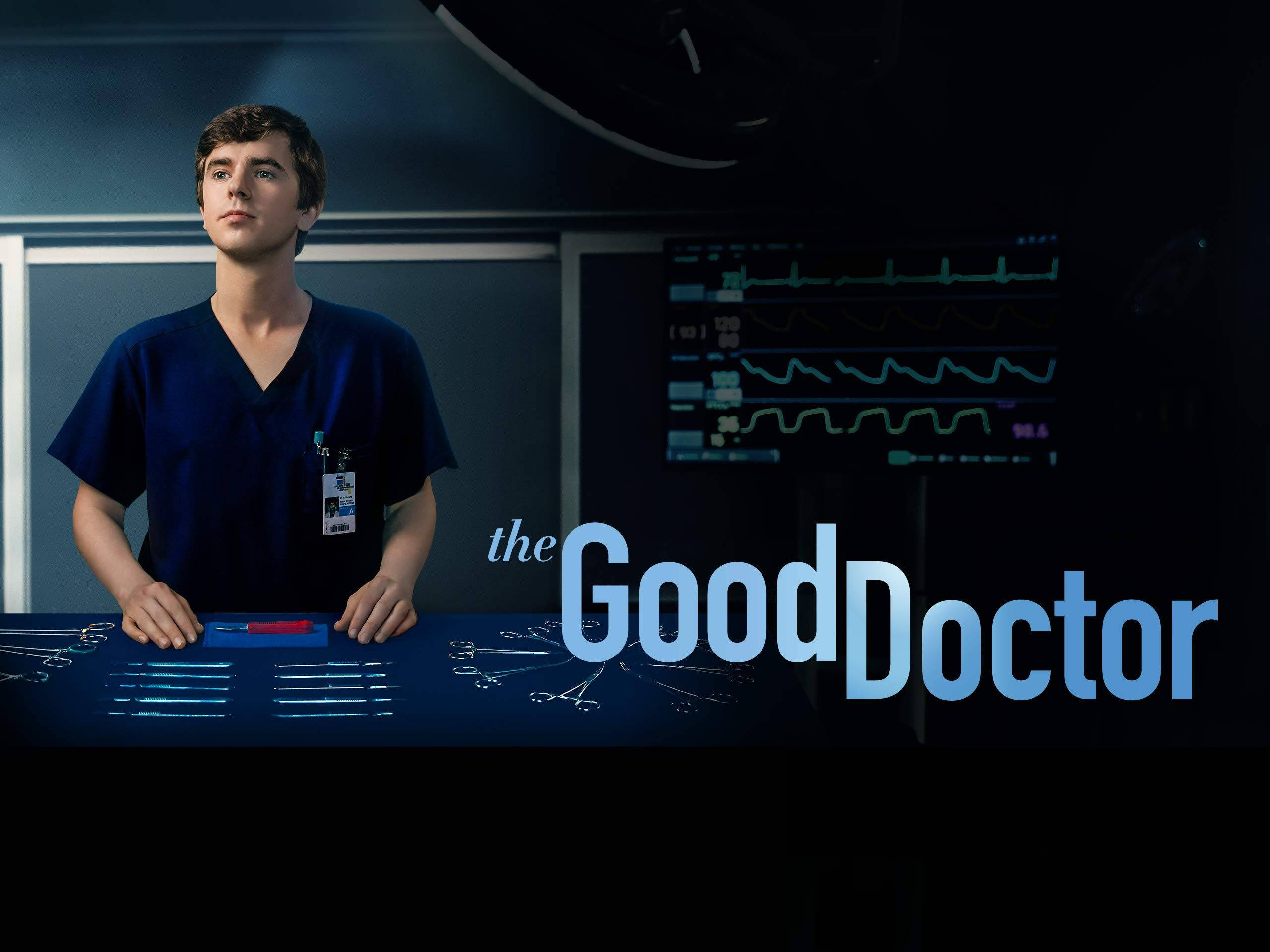The Good Doctor 桌布 壁紙 — 一位身穿藍色手術服的年輕醫生站在燈光昏暗的手術室中，周圍有醫療監視器和手術工具。
