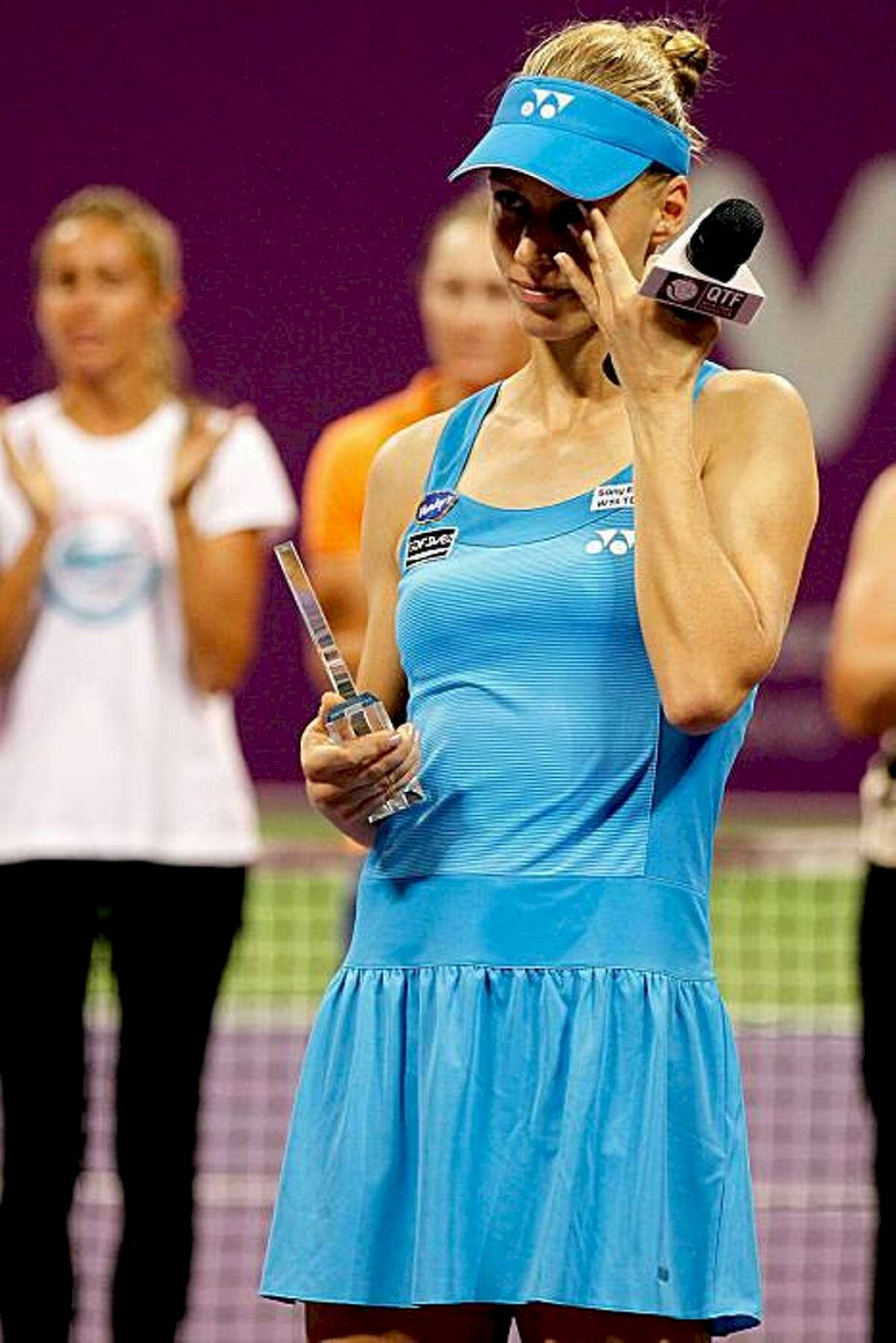 Athlete 桌布 壁紙 — 一位身穿藍色服裝的女網球選手在球場上接受訪問時，手持獎盃並擦拭眼睛。