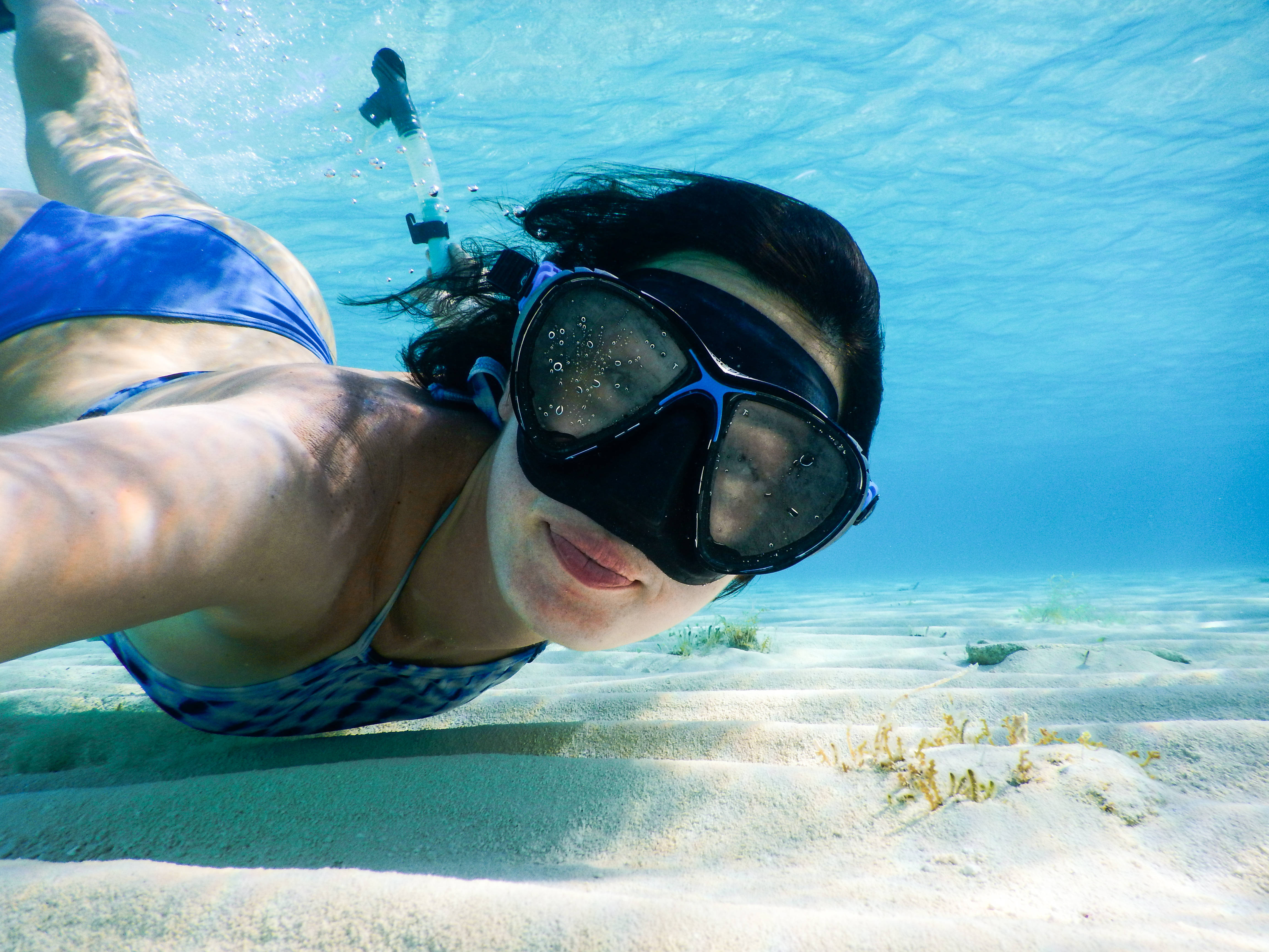 Snorkeling 桌布 壁紙 — 一位身穿藍色泳衣和潛水裝備的女性，在陽光照耀的沙質海底上優雅地滑行。