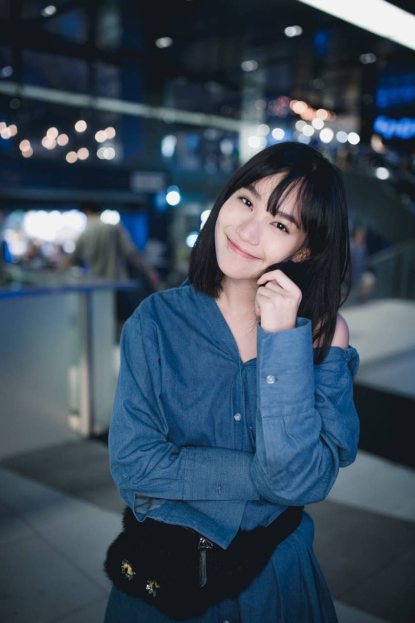 高清 桌布 壁紙 — 一位身穿藍色牛仔套裝的年輕女性，在柔和燈光的城市夜景中，背景燈光模糊，溫暖地微笑擺姿勢。