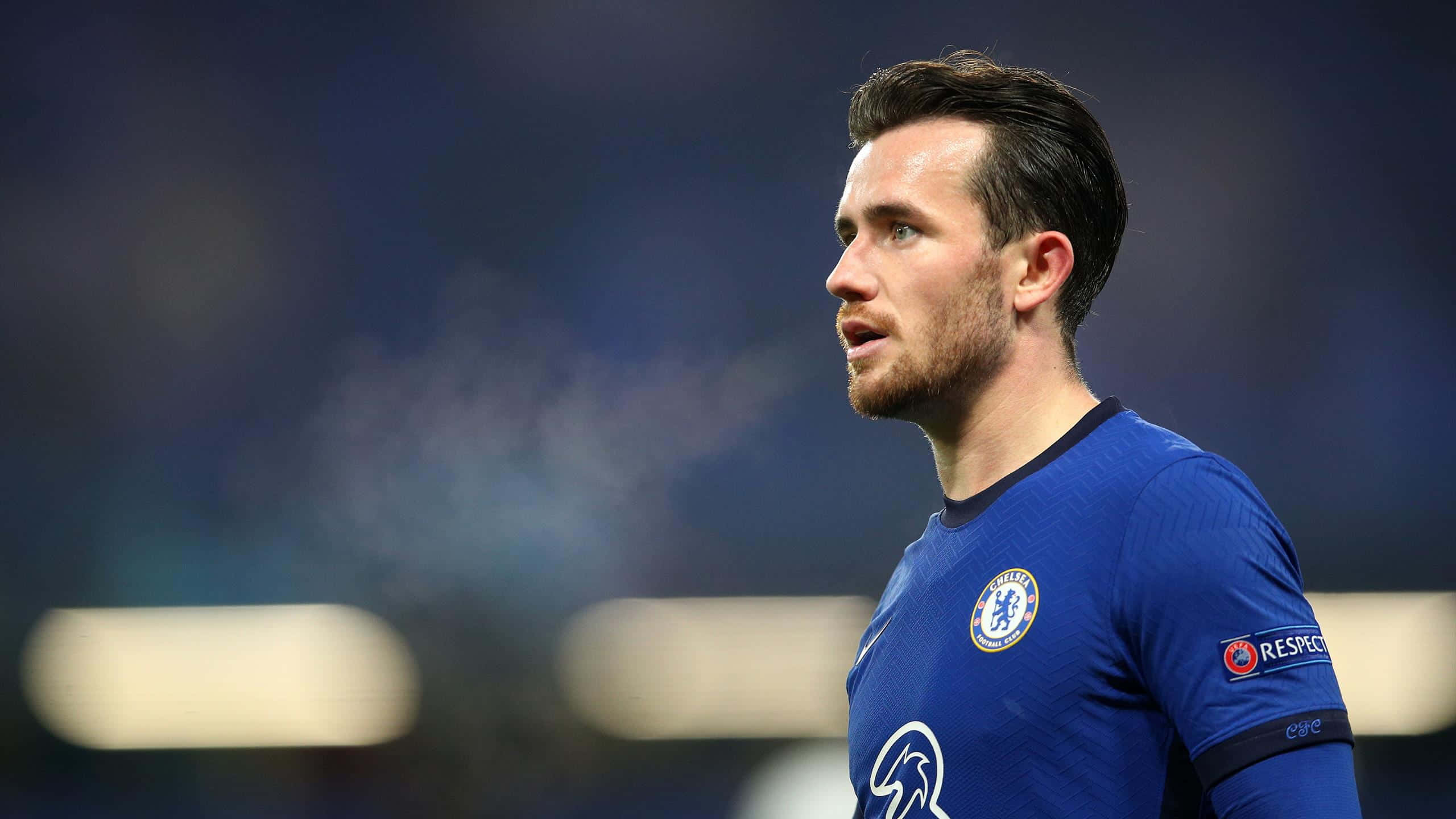 足球 桌布 壁紙 — 一位身穿藍色球衣、專注的切爾西足球員在夜間比賽中於球場燈光下凝視著。